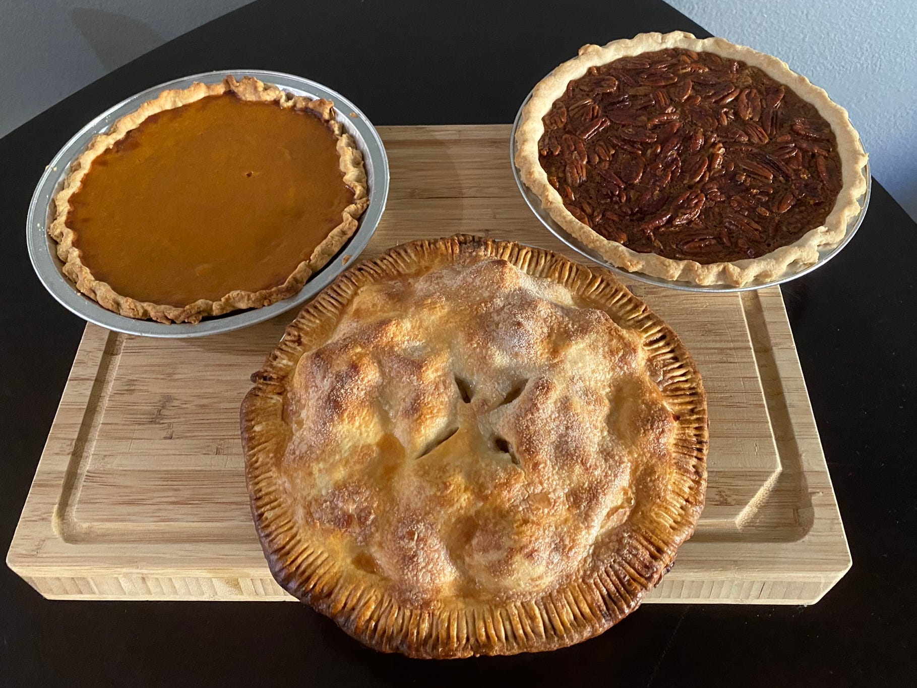 a pumpkin pie, an apple pie, and a pecan pie on a kitchen cutting board