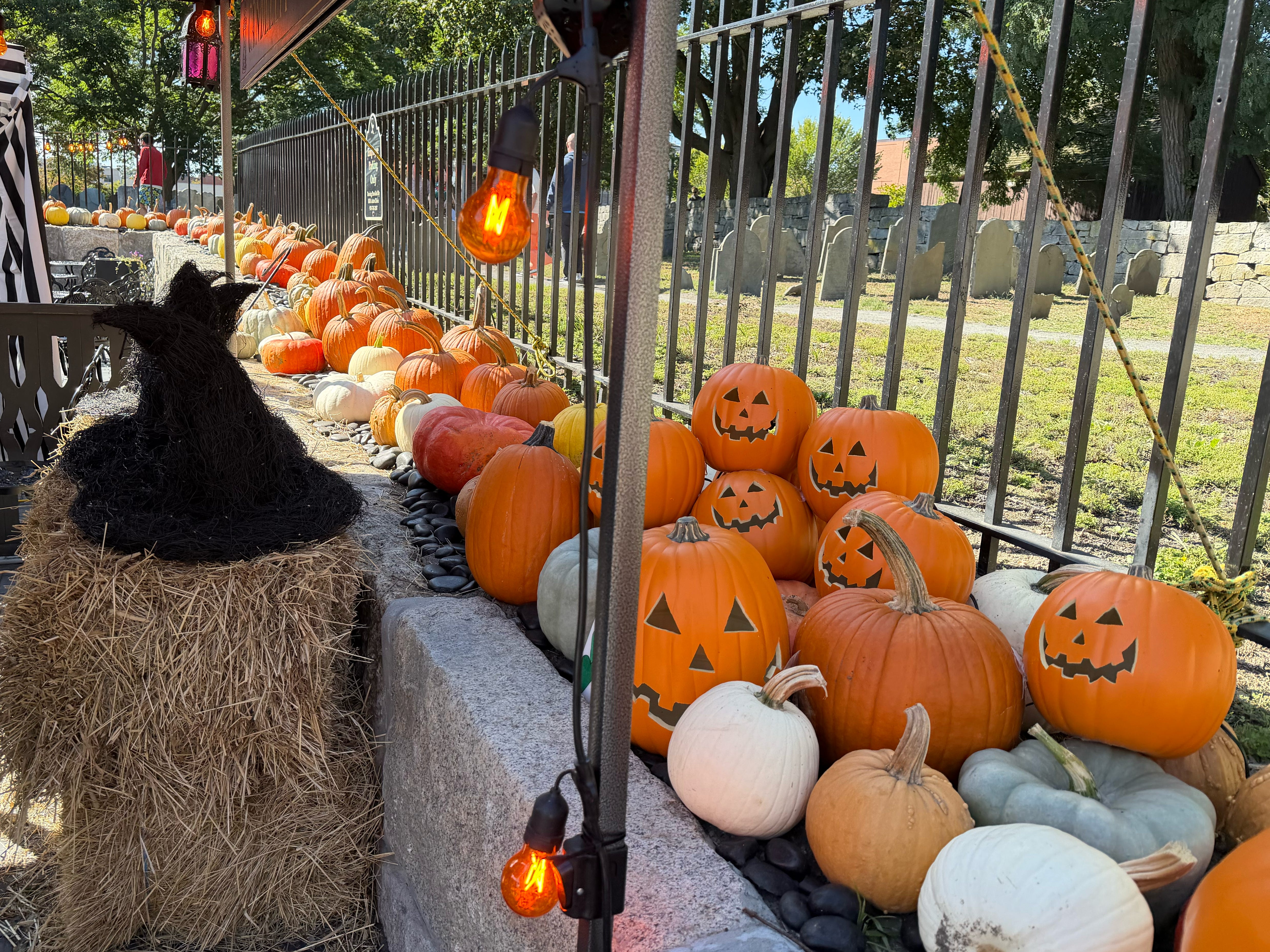 Pumpkins and jack-o'-lanterns on a rock wall with a graveyard in the back.