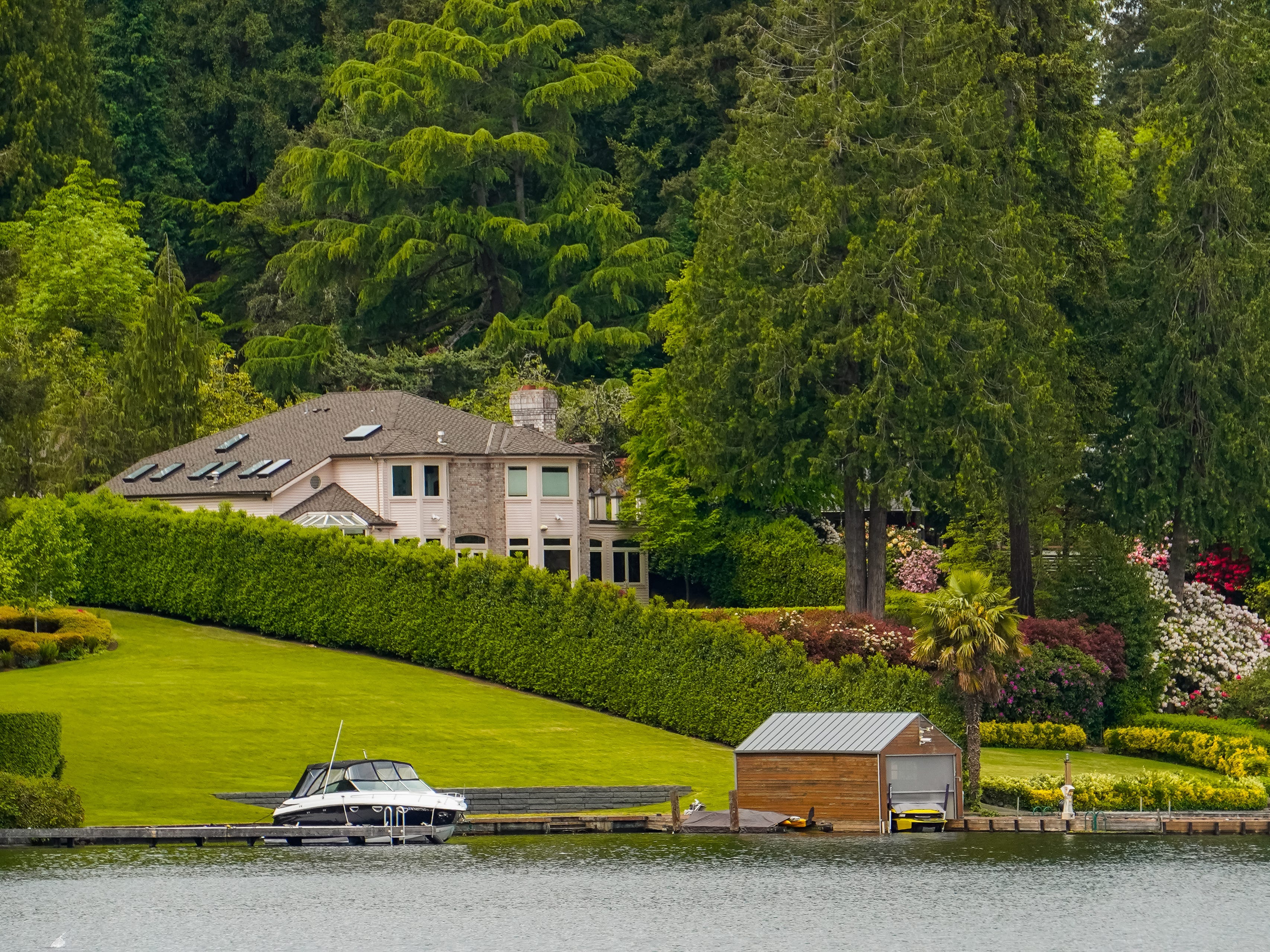 A mandion surrounded by trees next to a body of water with a boat docked on the left