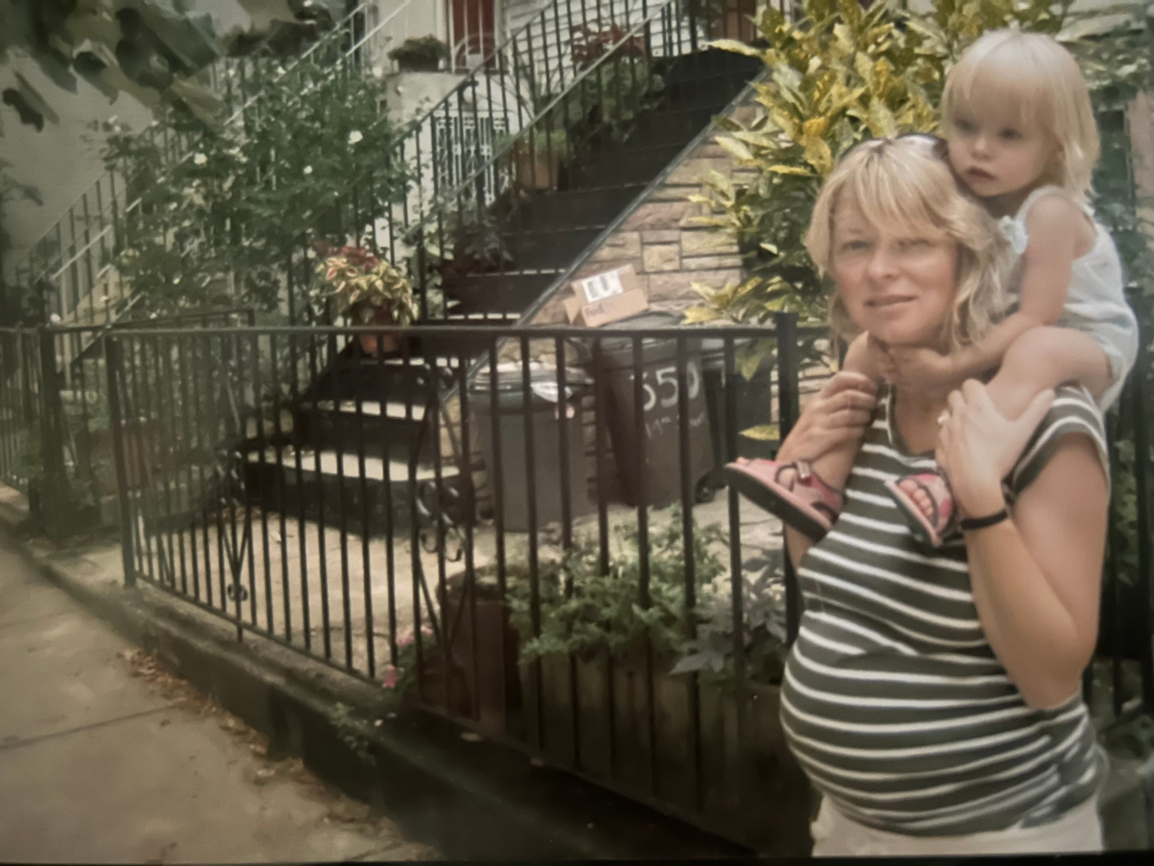 A pregnant woman on a street carrying a toddler on her shoulders