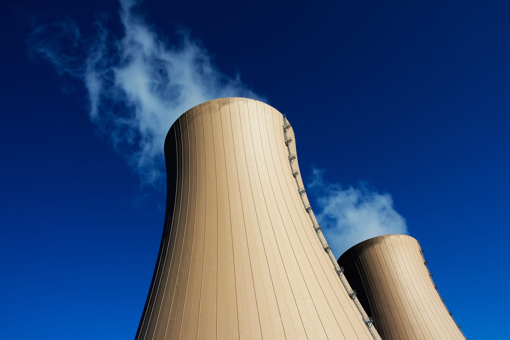 The towers of a nuclear power plant releasing steam against a blue sky.