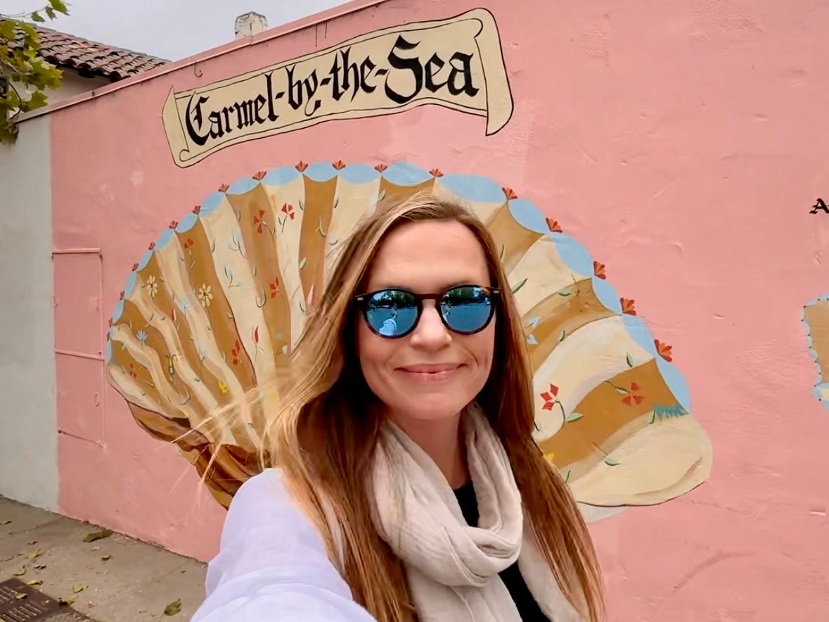 Emily taking a selfie in front of a pink Carmel-by-the-Sea mural.