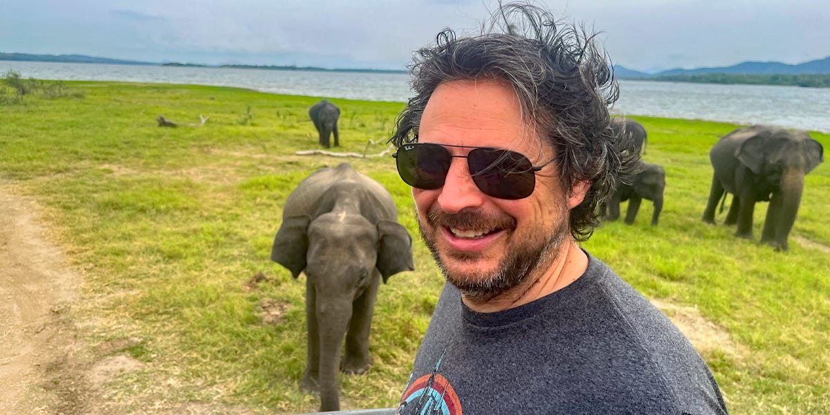 Author Ash Jurberg smiling in front of elephants