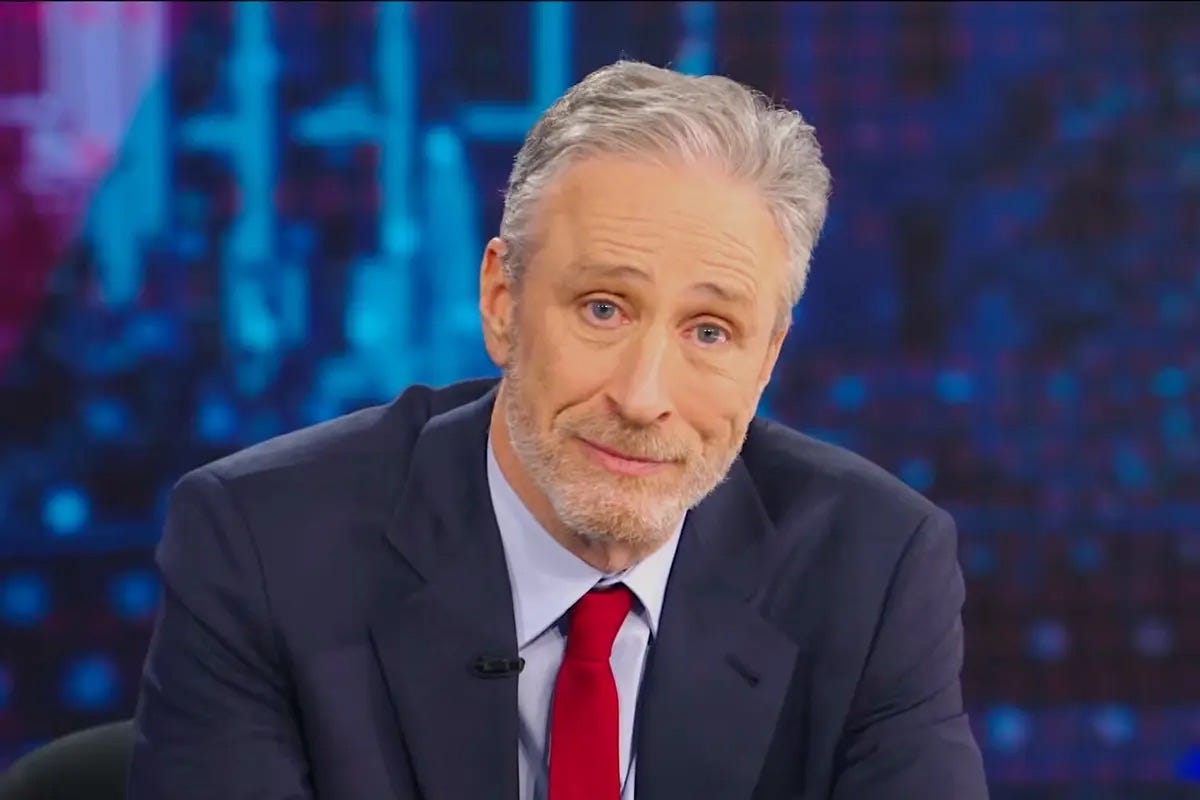 Jon Stewart is wearing a suit and looking ahead.