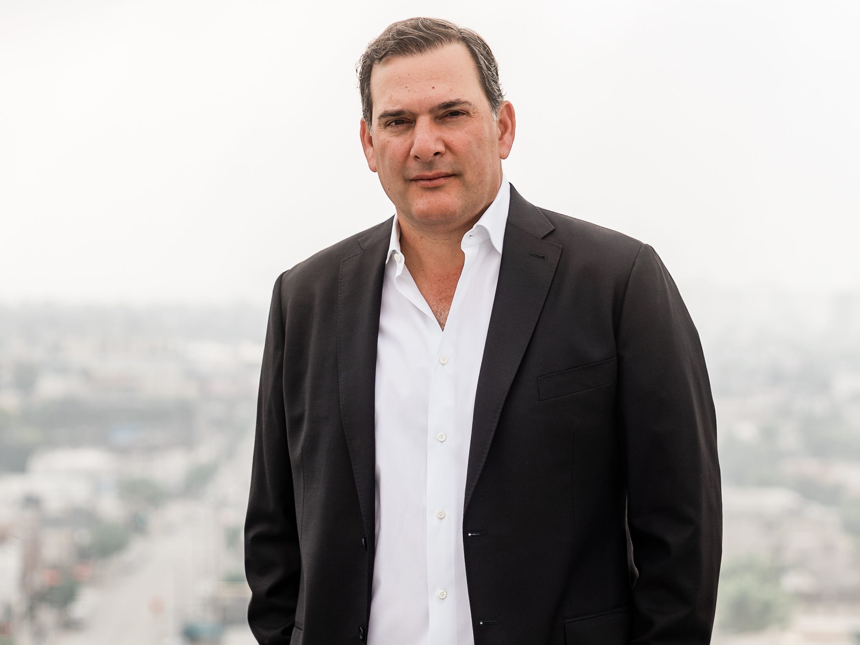 A man wearing a suit stands on a rooftop.