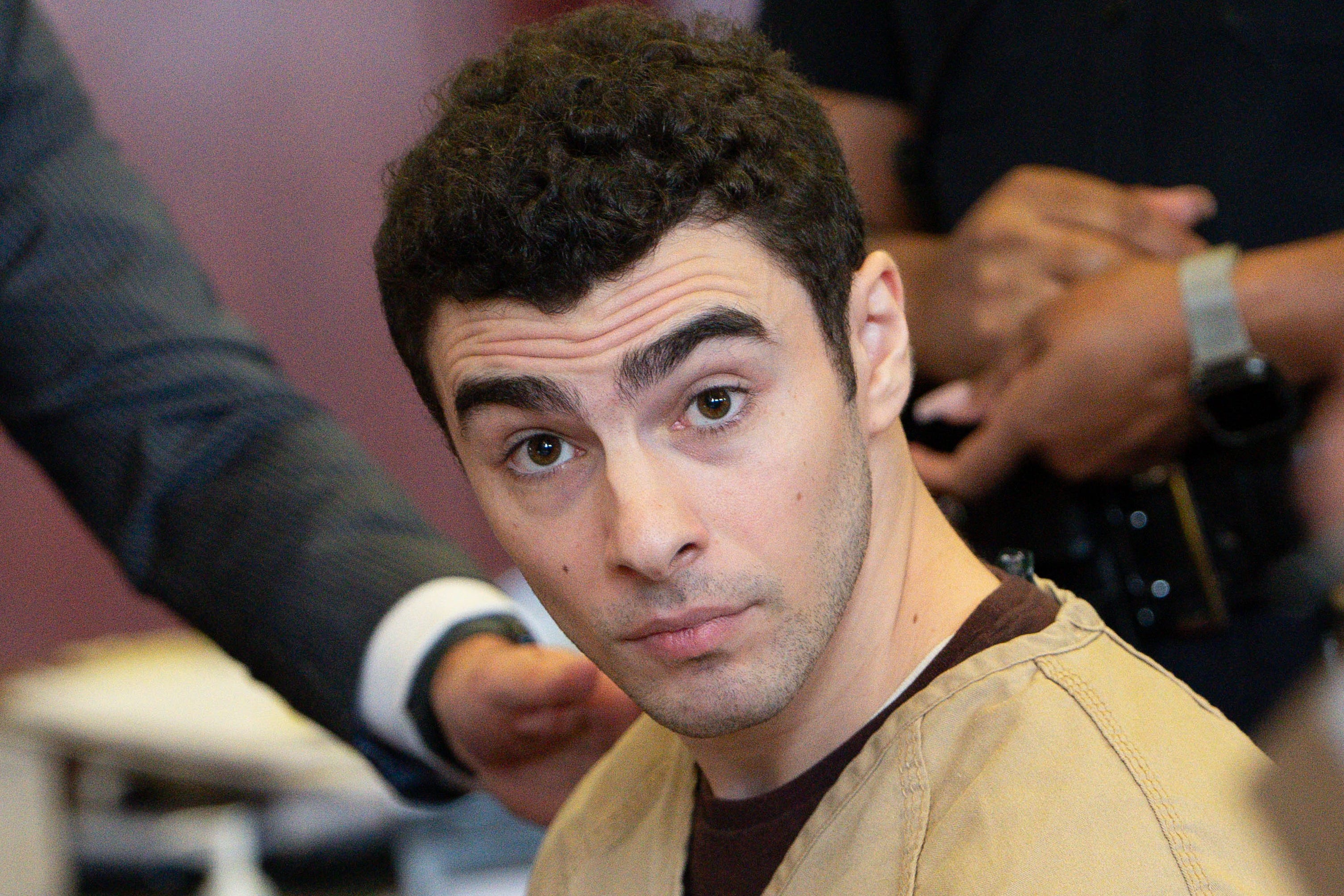 Luigi Mangione, charged in the murder of UnitedHealthcare CEO Brian Thompson, wears a tan prison smock and looks at the camera during a court appearance in Manhattan.