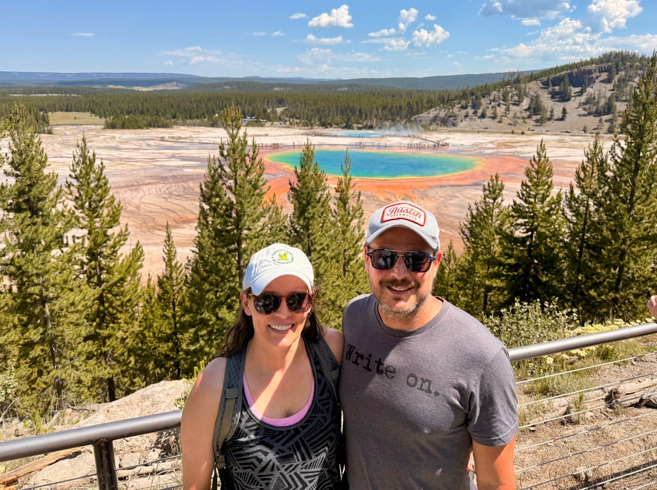 Author Ash Jurberg and wife smiling in front of Grand Prismatic Springs