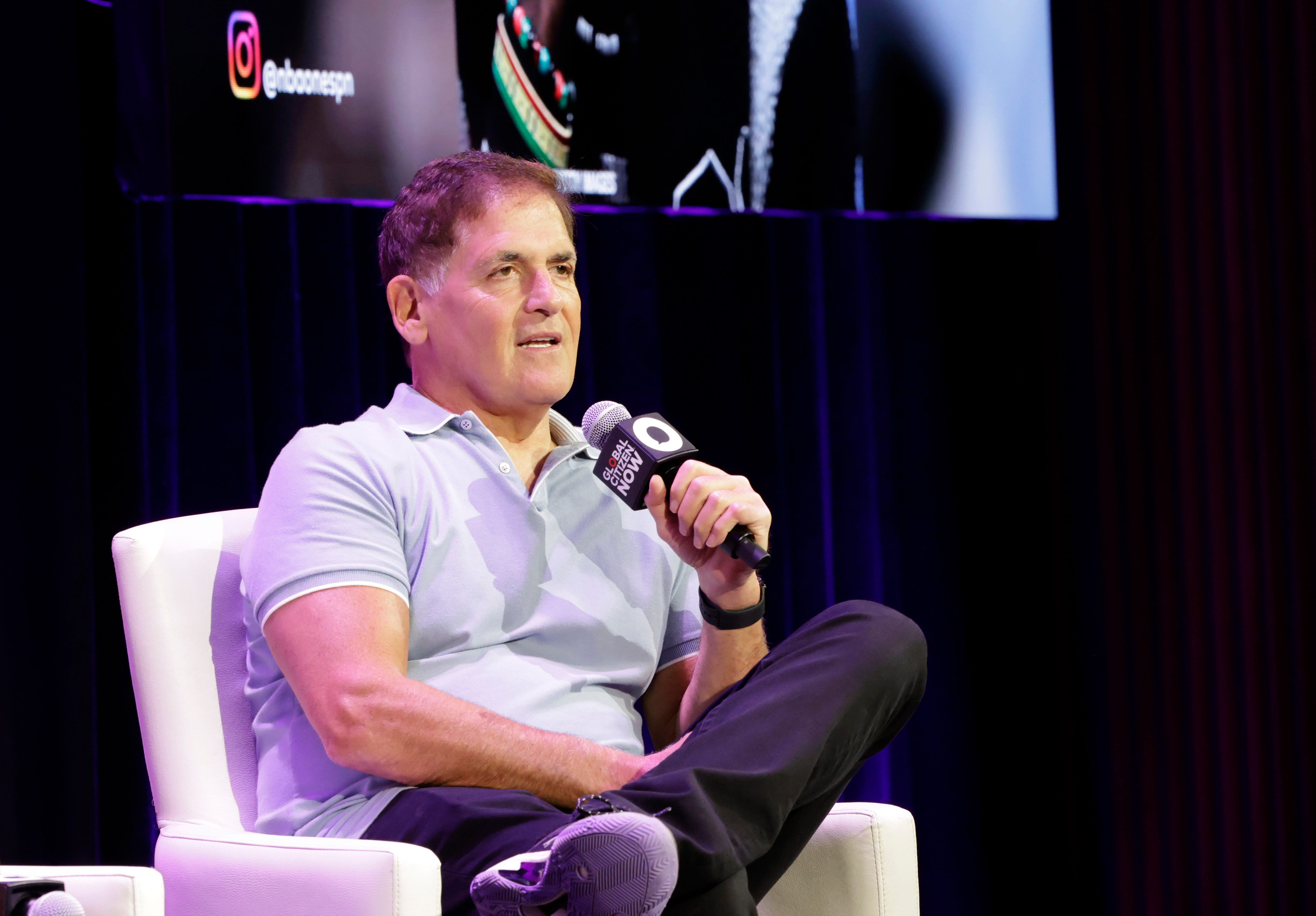 Mark Cuban is sitting on a white sofa and speaking into a microphone.