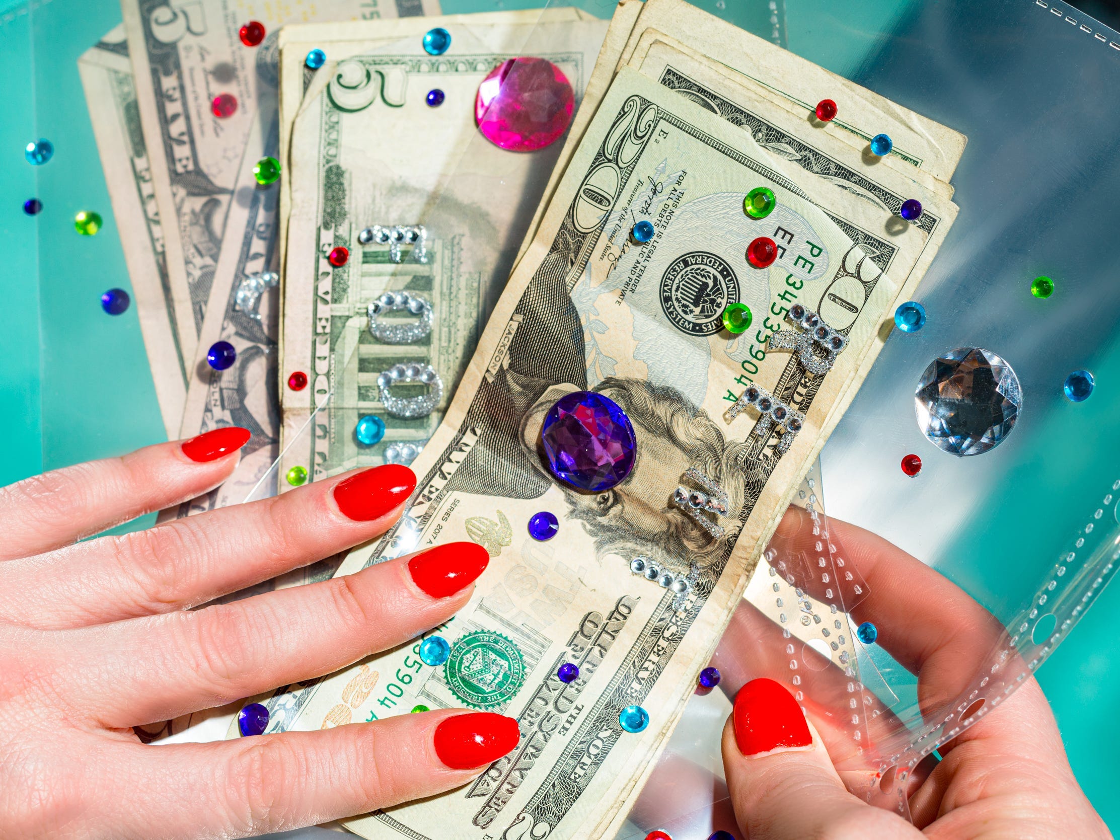 A woman with acrylic nails holding cash, plastic envelopes, and rhinestones