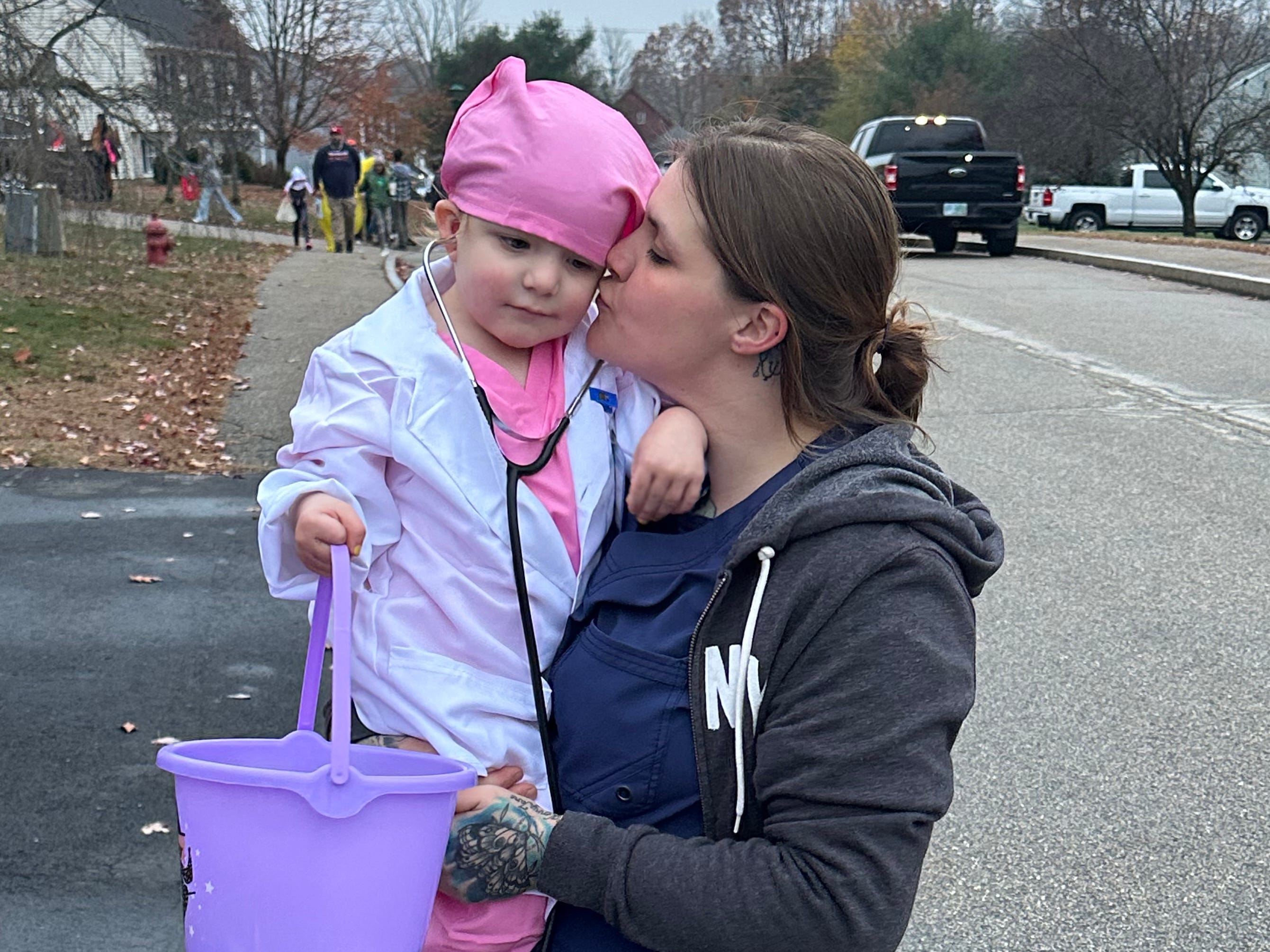 A woman kisses her toddler daughter, who is dressed in scrubs for Halloween.