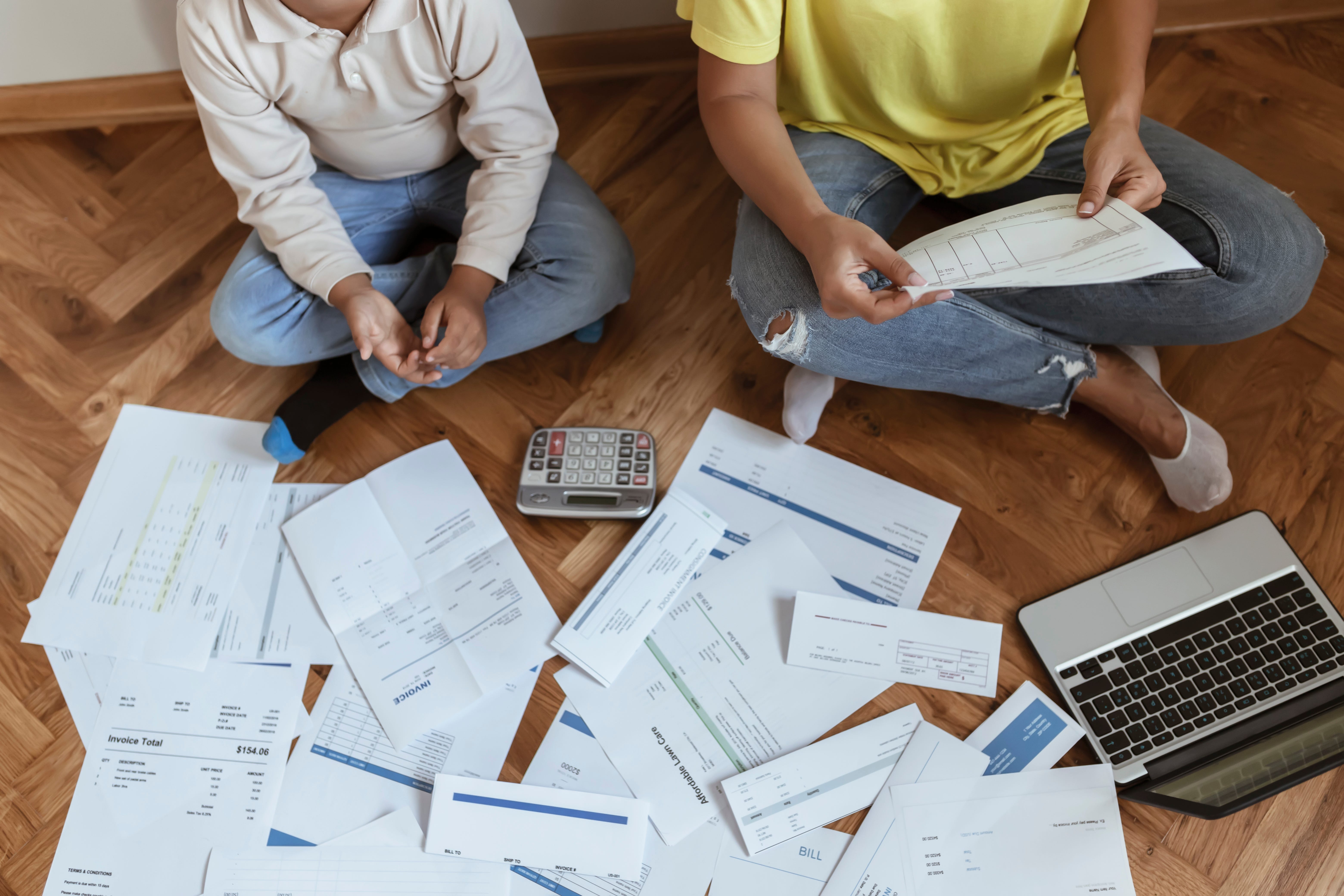 Two people sit on the floor while bills appear to be spread out around them.