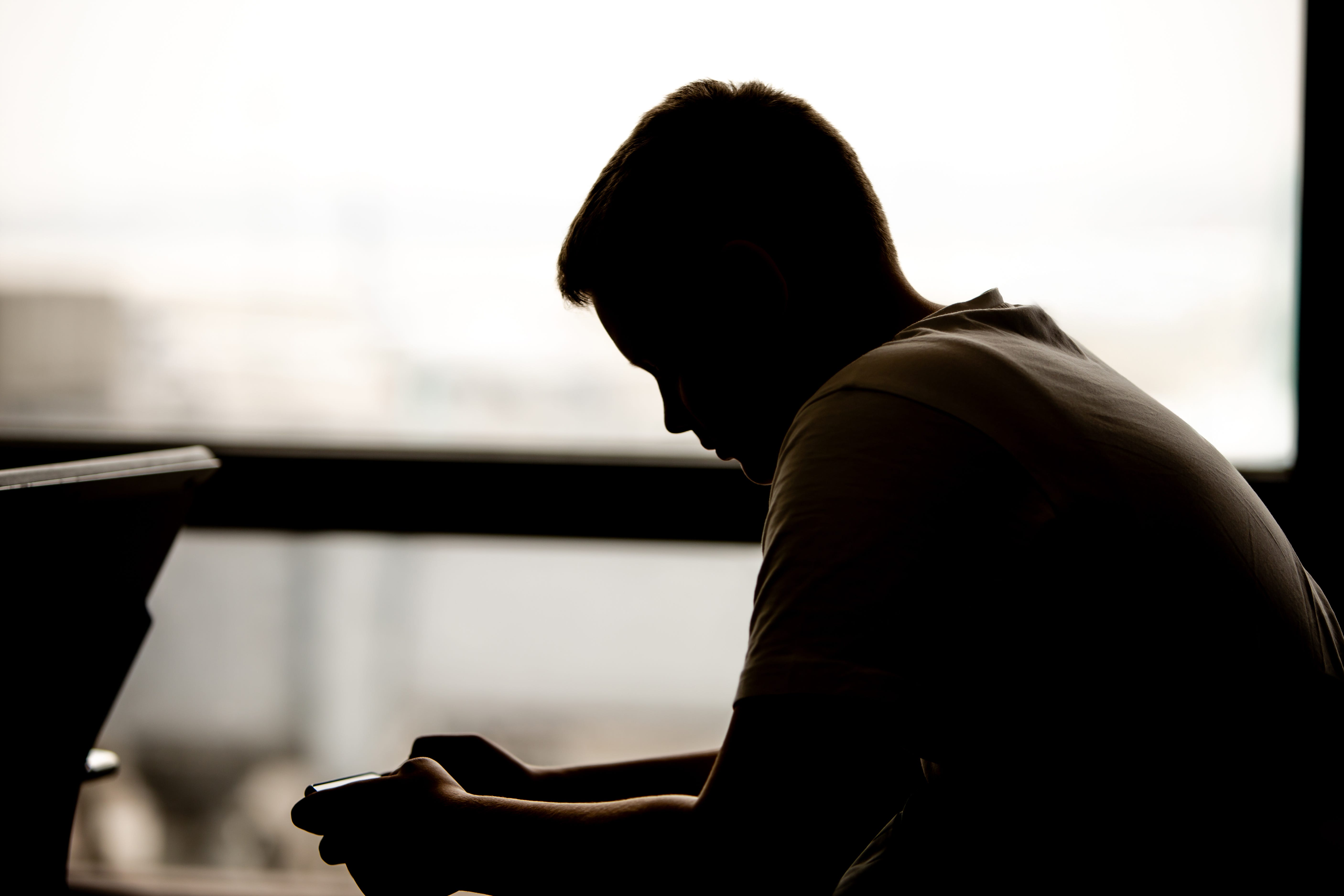 A young teen boy is sitting on a bench looking at his phone.