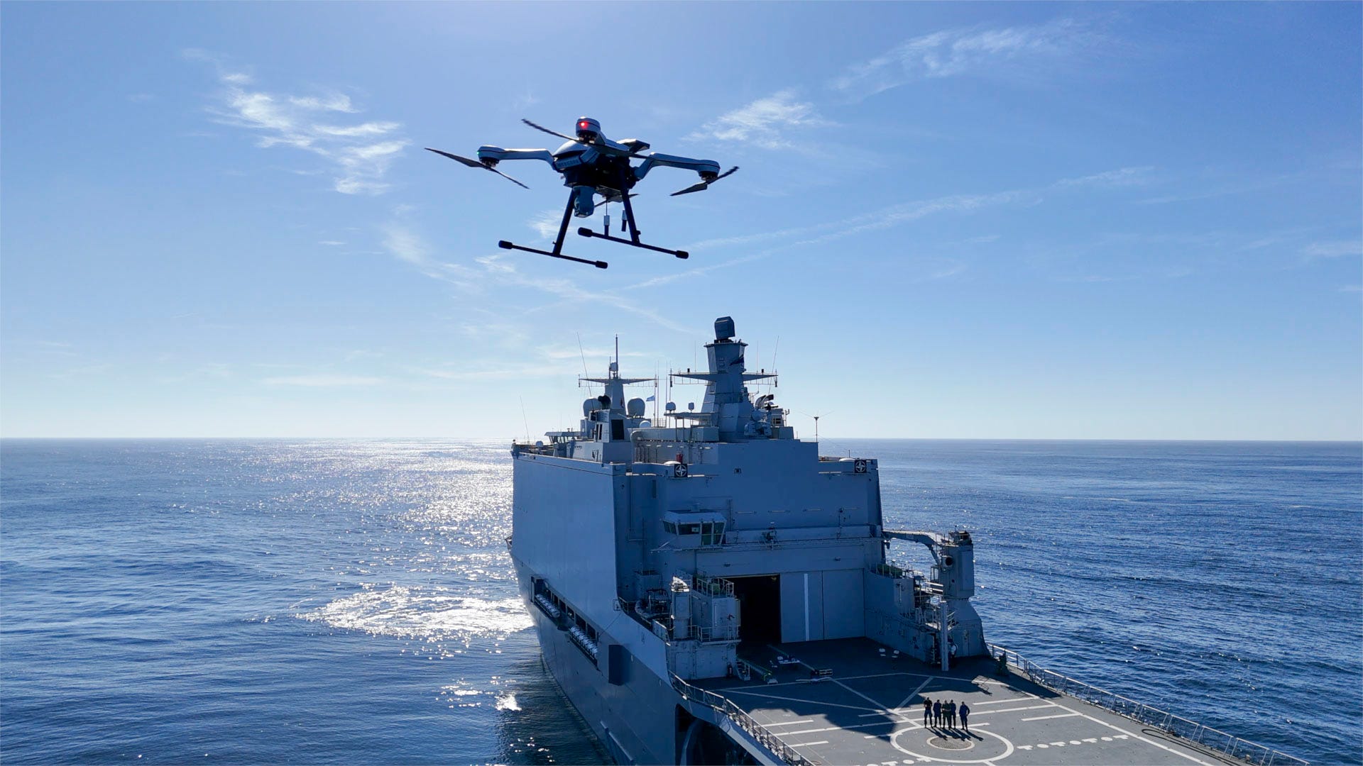 A drone hovers near a military ship.