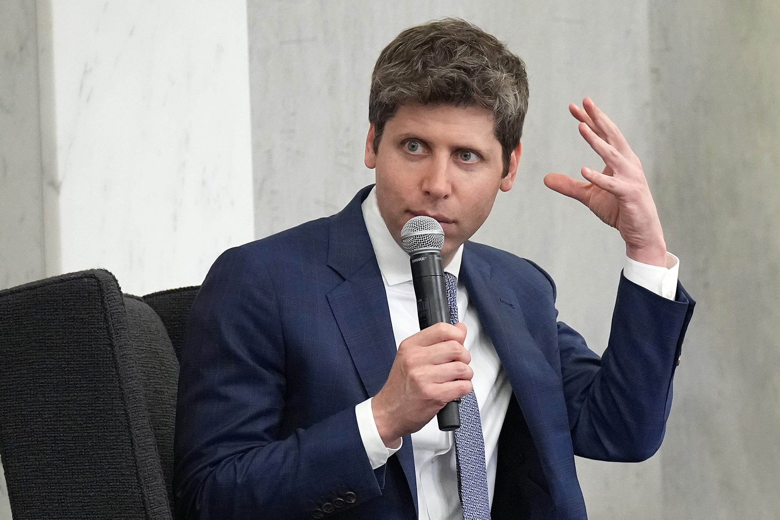 Sam Altman motions toward his head while speaking with a microphone