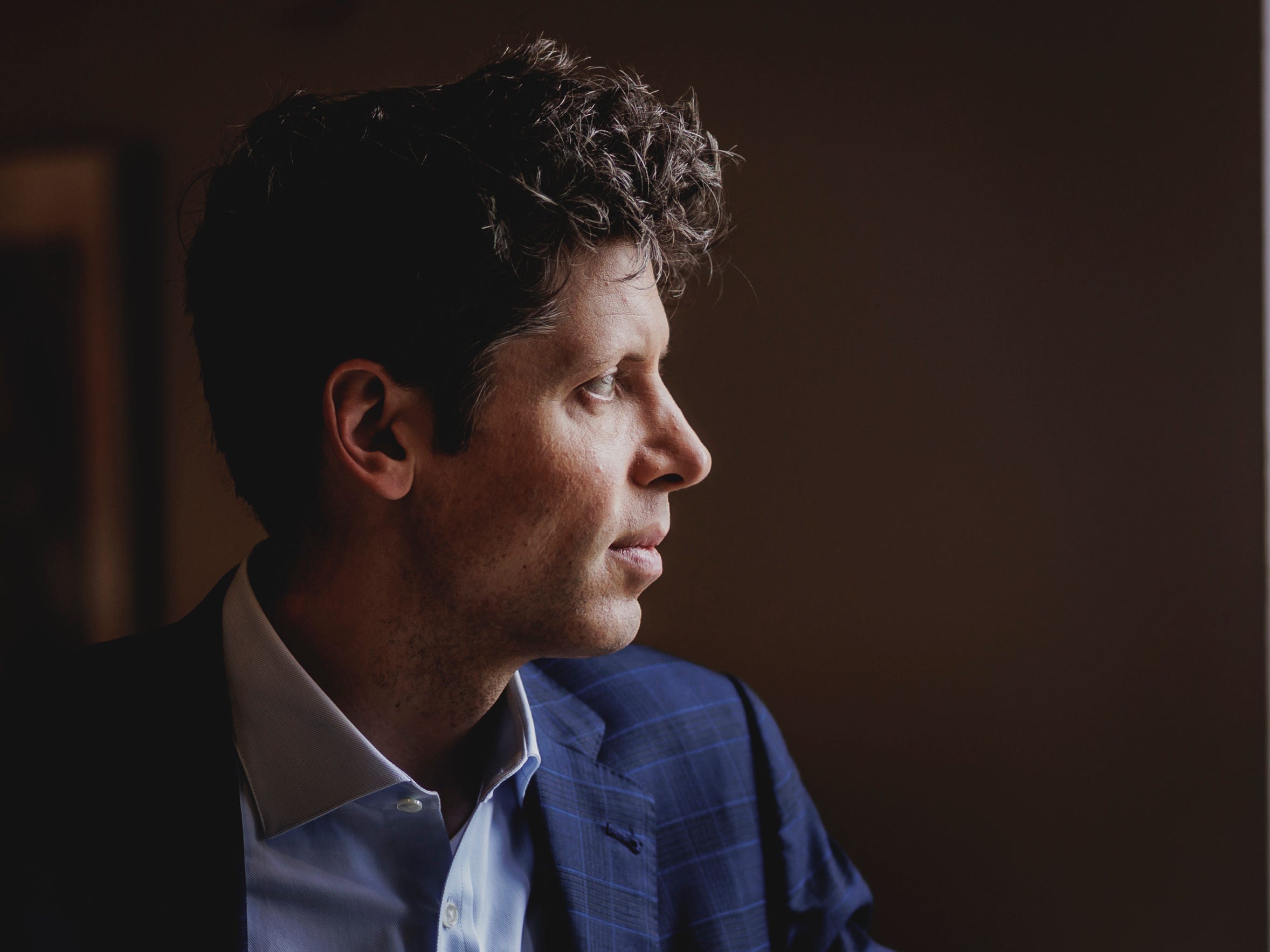 Sam Altman's profile, standing in front of a window.