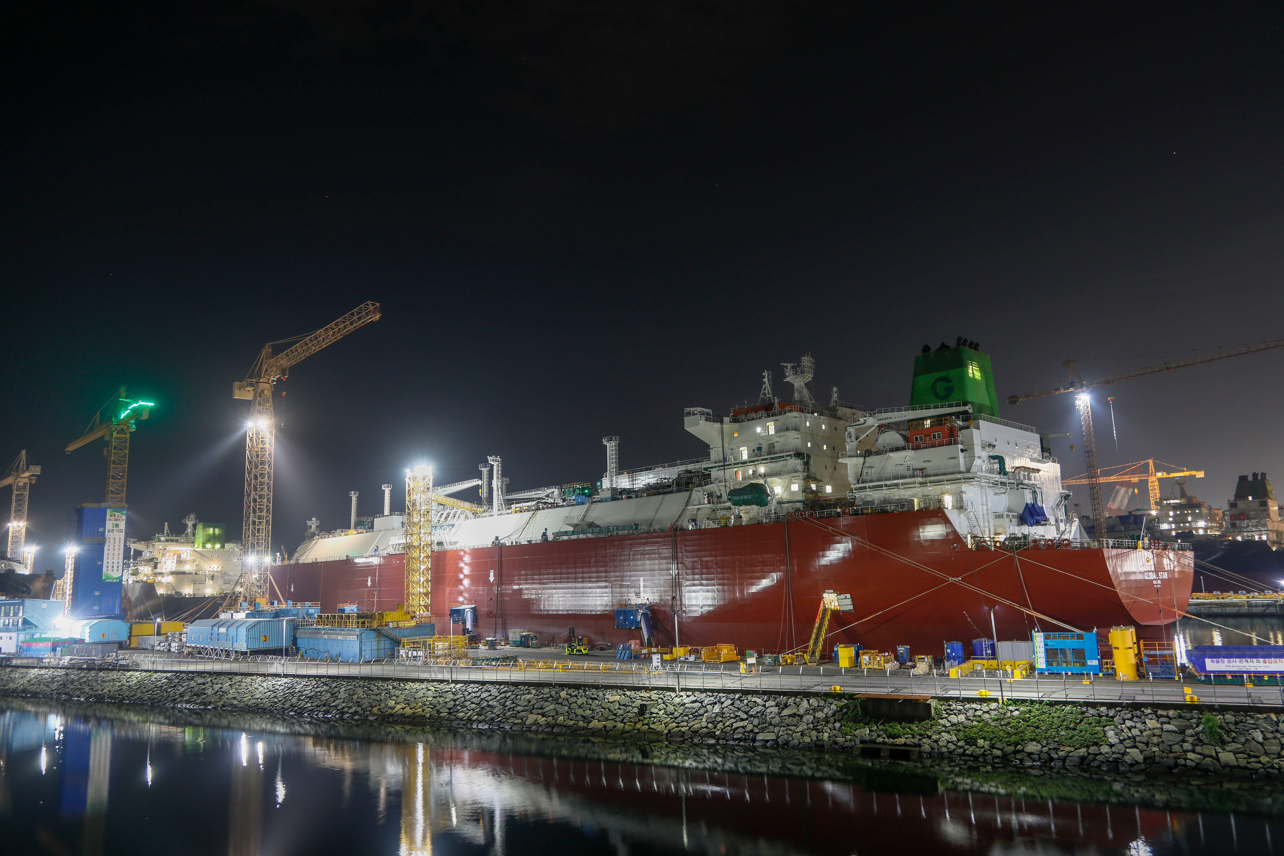 A large ship with a red hull is sitting in a dry dock at a shipyard at night.