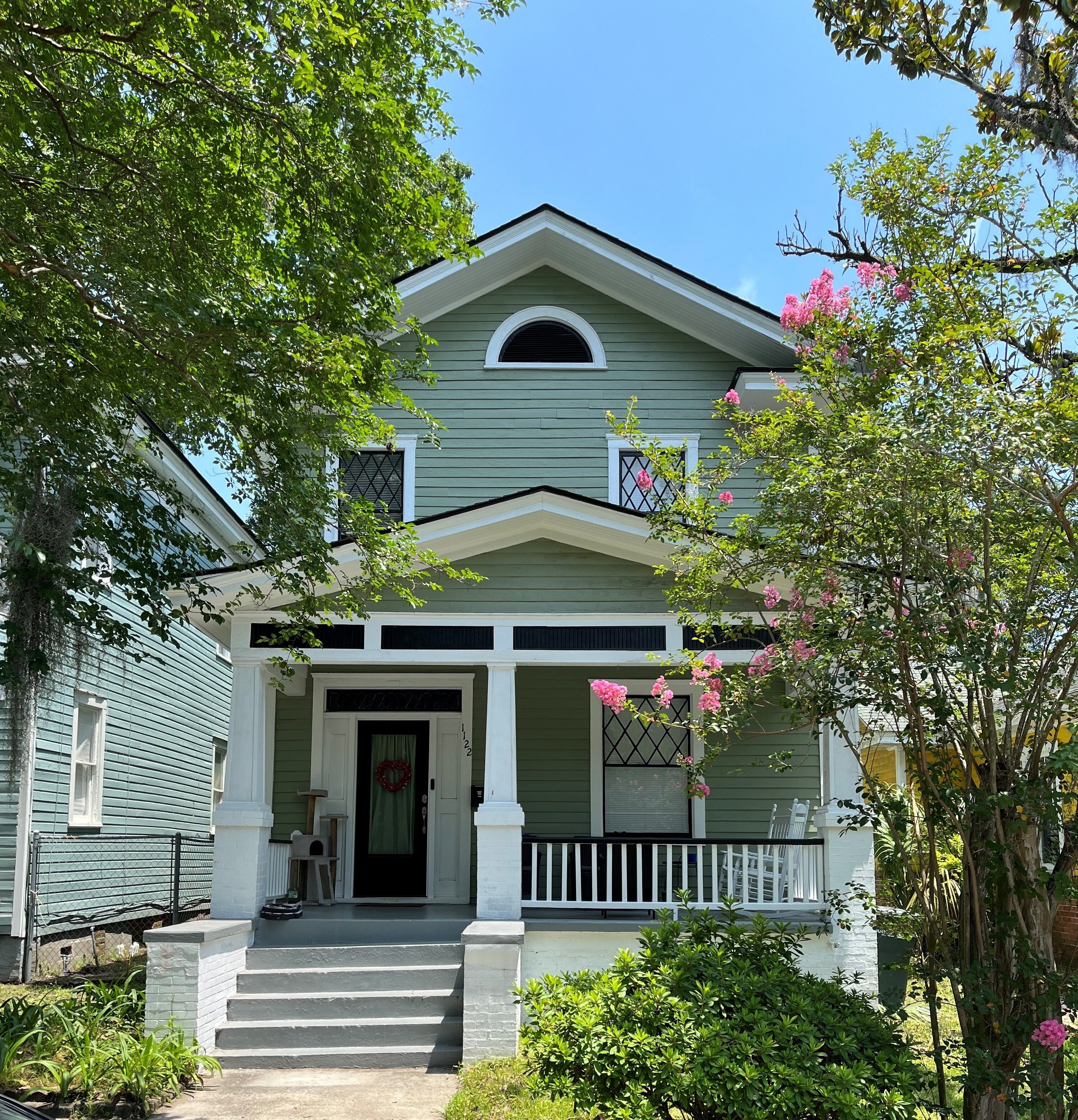 A green townhome on a leafy street.
