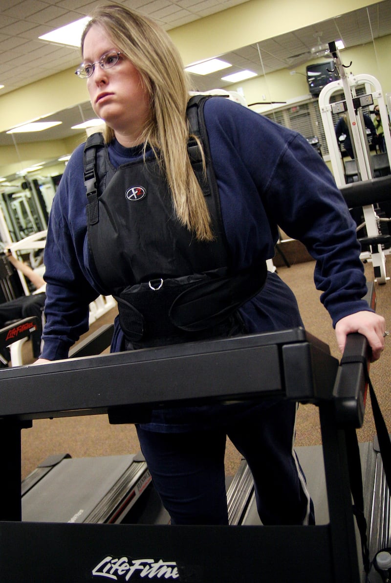 A Woman using a weighted vest while on a  treadmill.