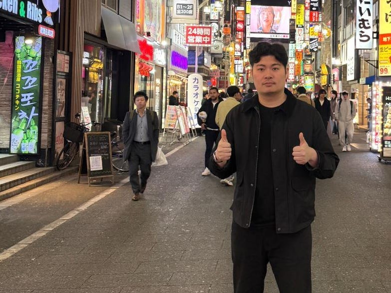 Eric Fung  standing on a street in Tokyo with Japanese writing on the signs.
