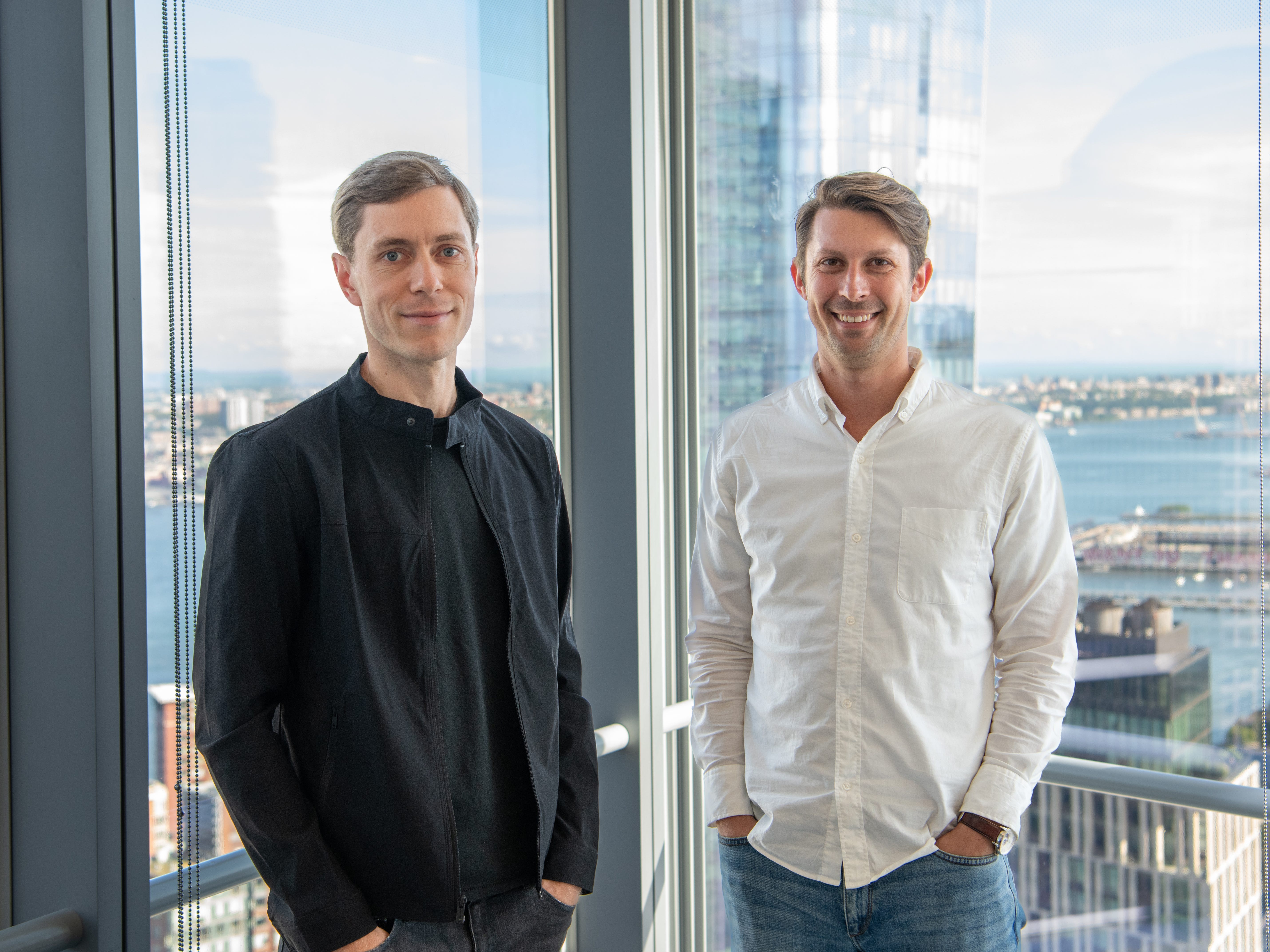 Spara cofounders David Walker and Zander Pease, standing in front of glass windows with a city skyline behind them.