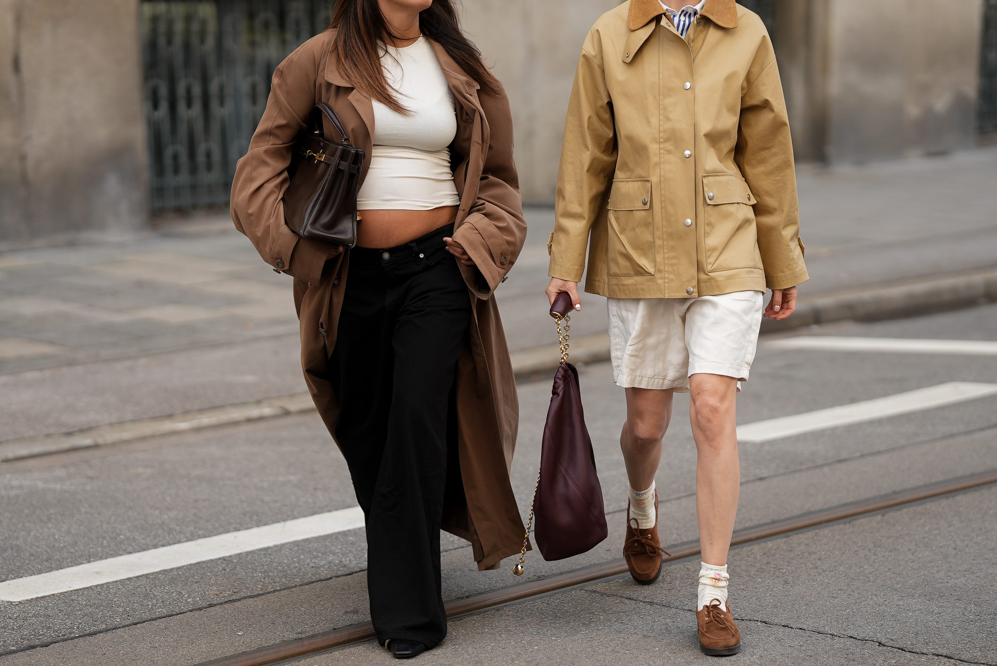 Two people walking - one wearing barn jacket and shorts, another wearing long coat and crop top