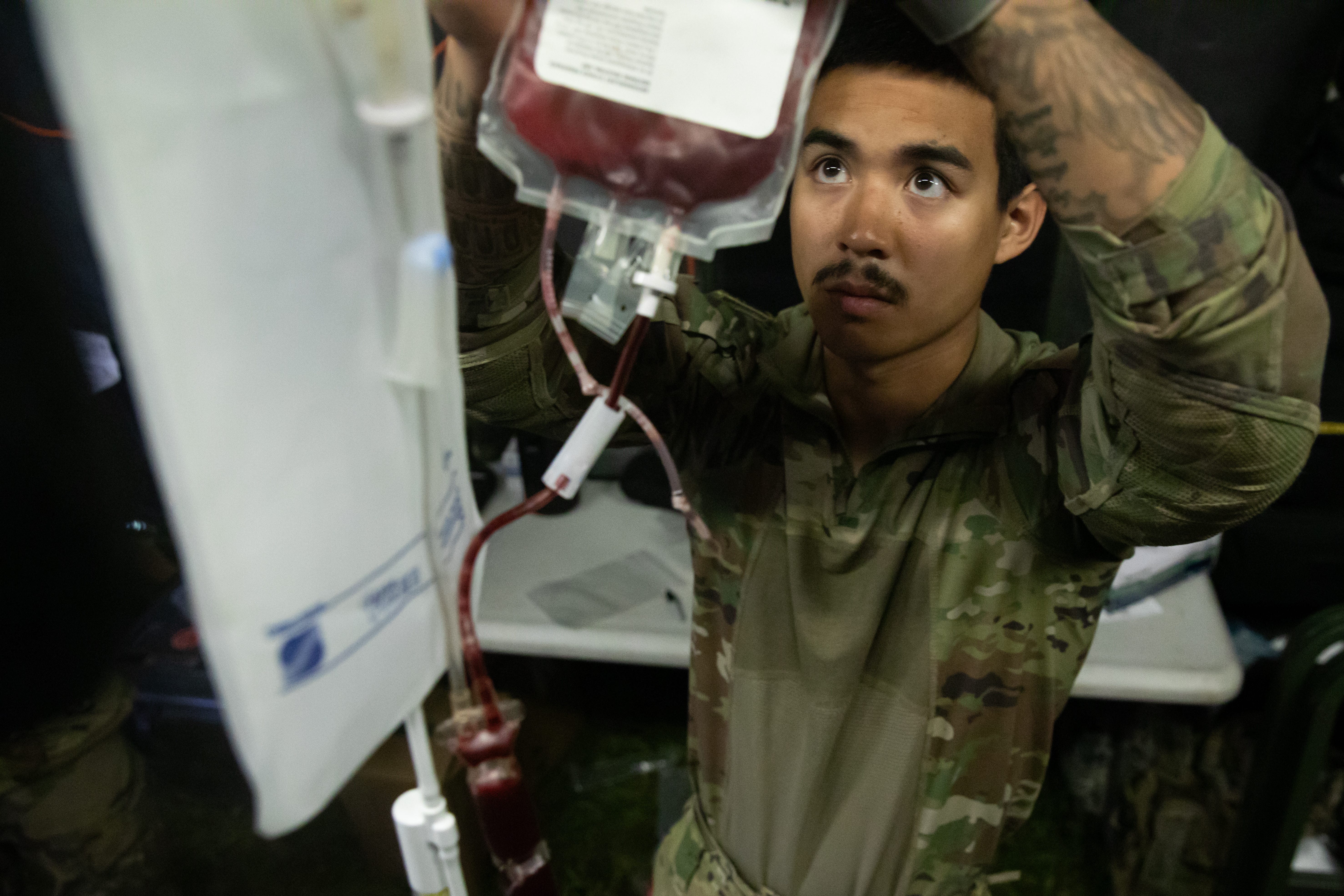 A man in camouflage is working on a bag of blood.