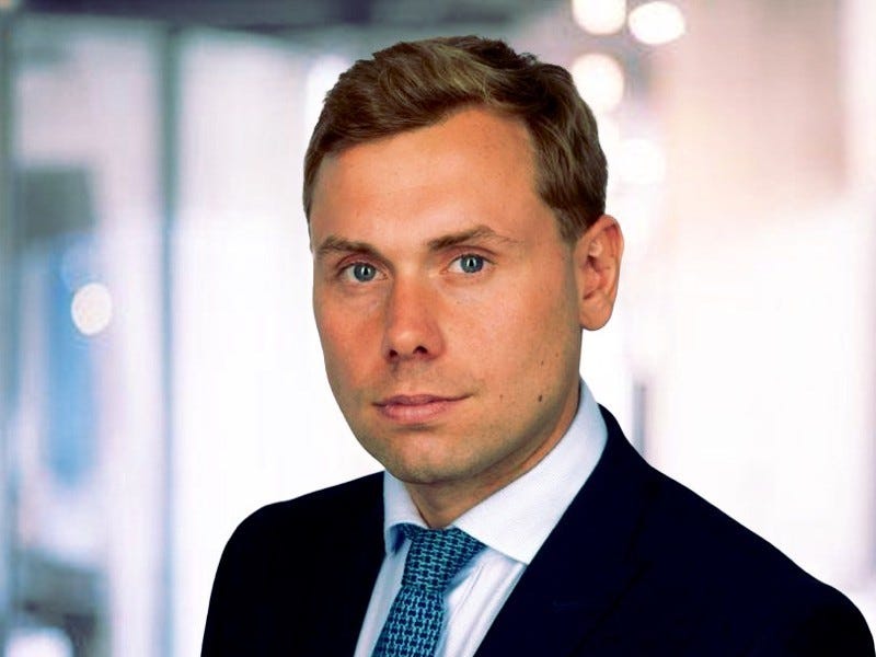 Caspar Macqueen stands in front of an office backdrop