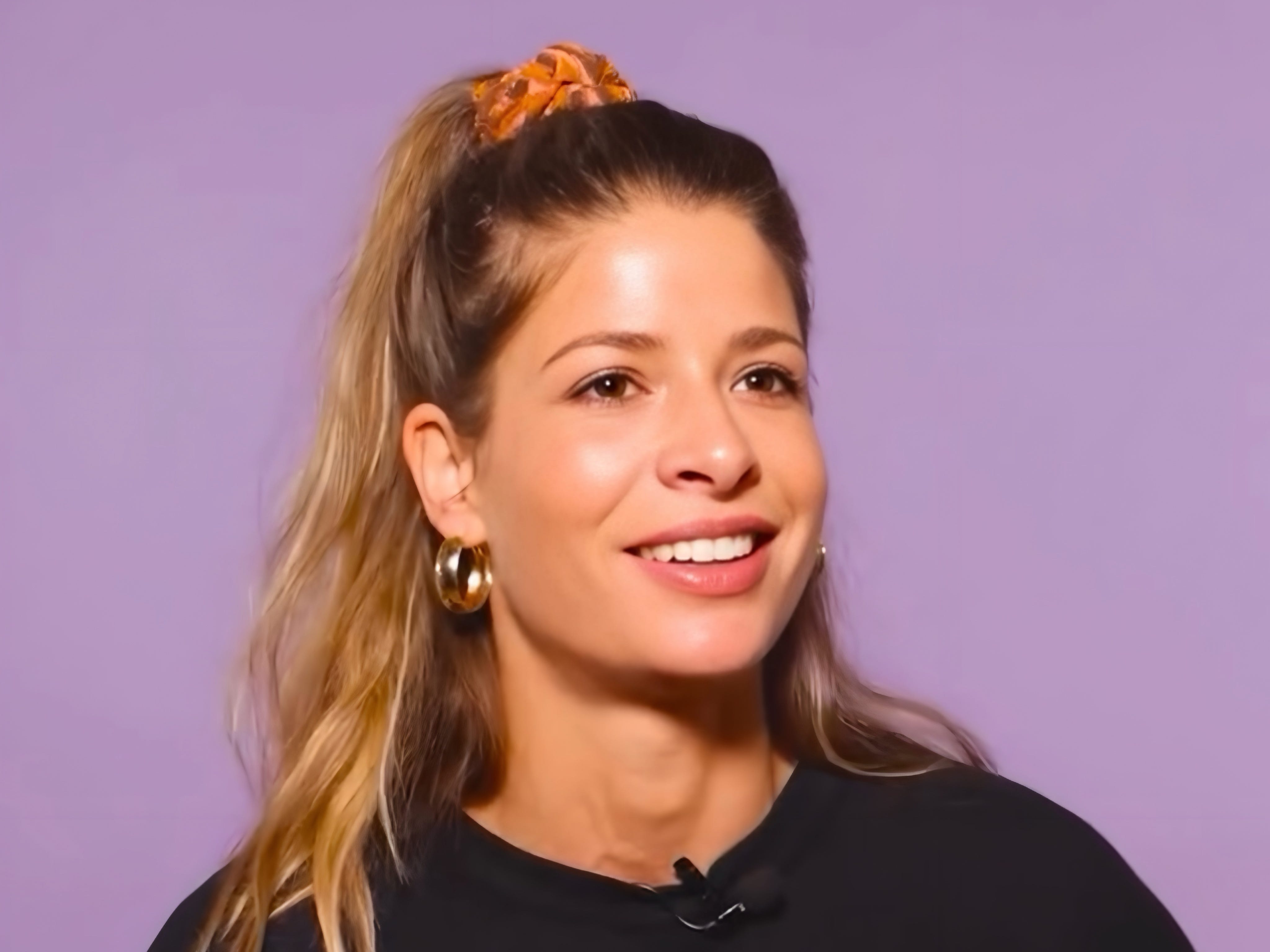 Clara Gold, a female founder, smiling in front of purple background wearing black shirt