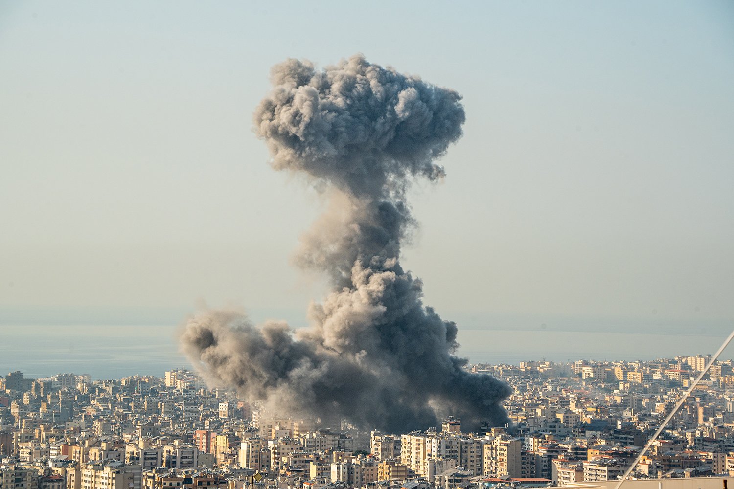 A large cloud of smoke rises above the buildings of a city.