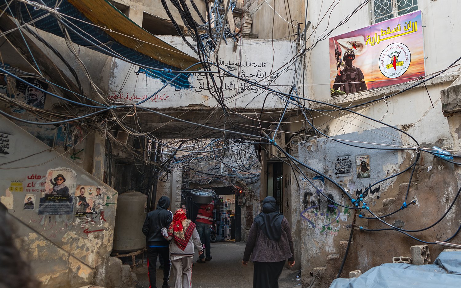 A person walks during a tangle of power lines between buildings with propaganda posters on the sides.