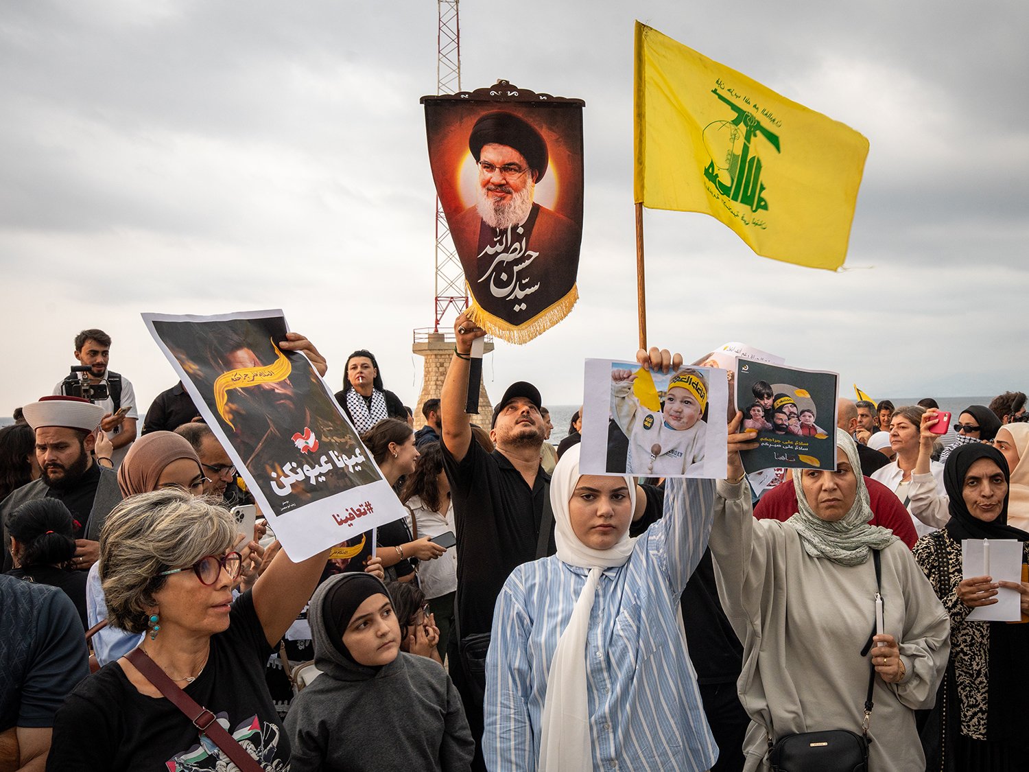 A cluster of people including a woman with a white headscarf hold up signs and flags as they march.
