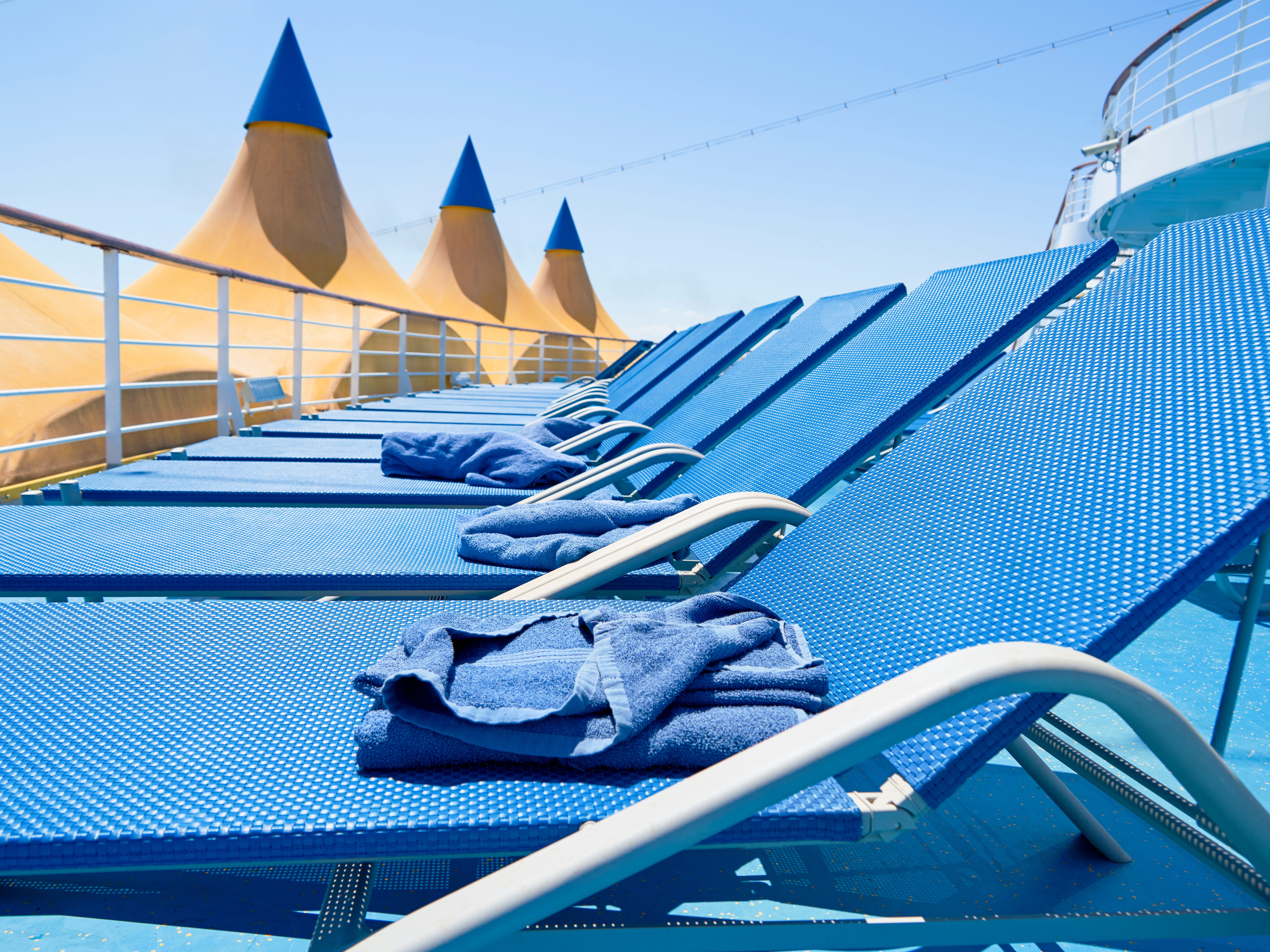 Blue lounge chairs lined up with towels on each one.