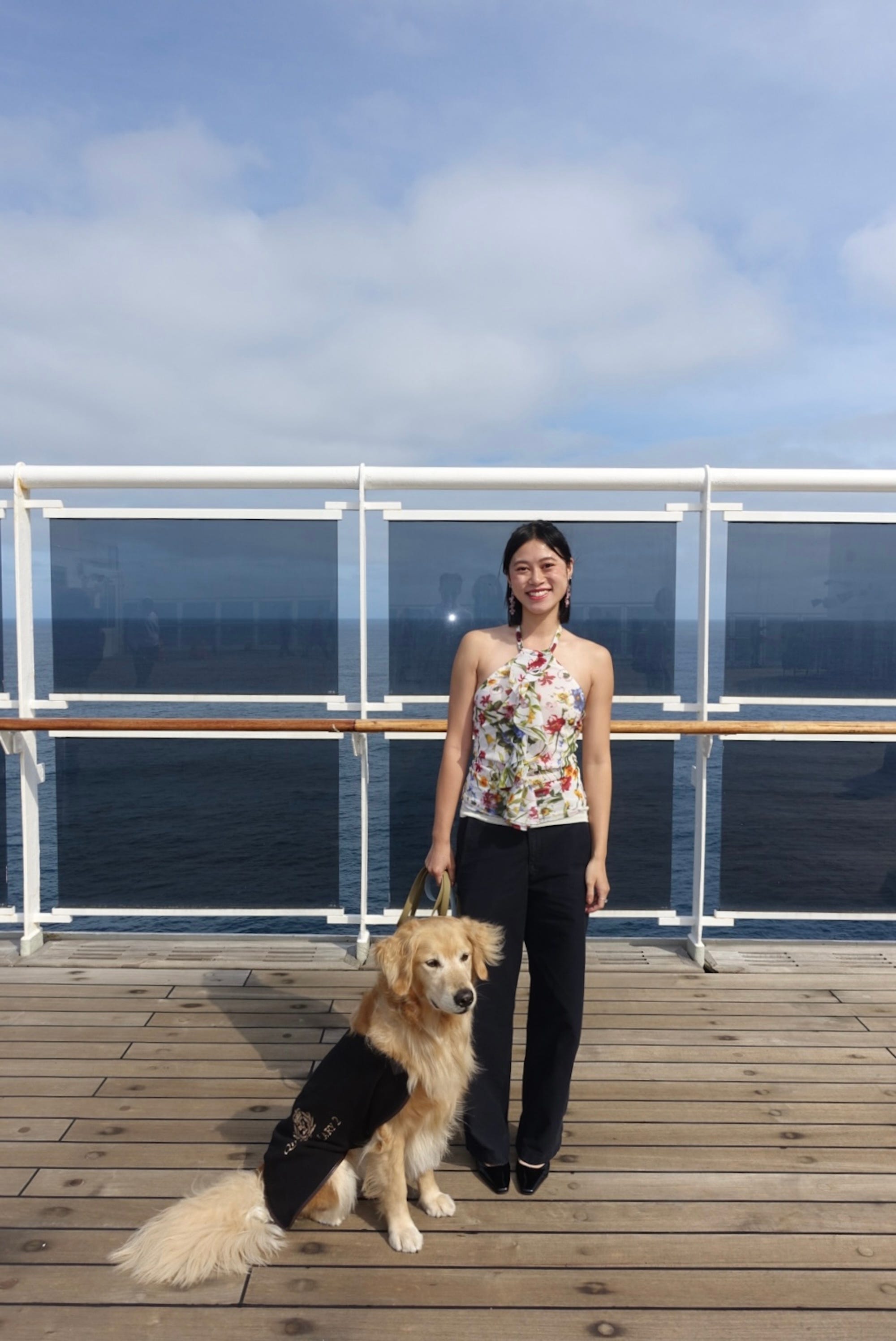 A woman and her dog stand together on the deck of a cruise.