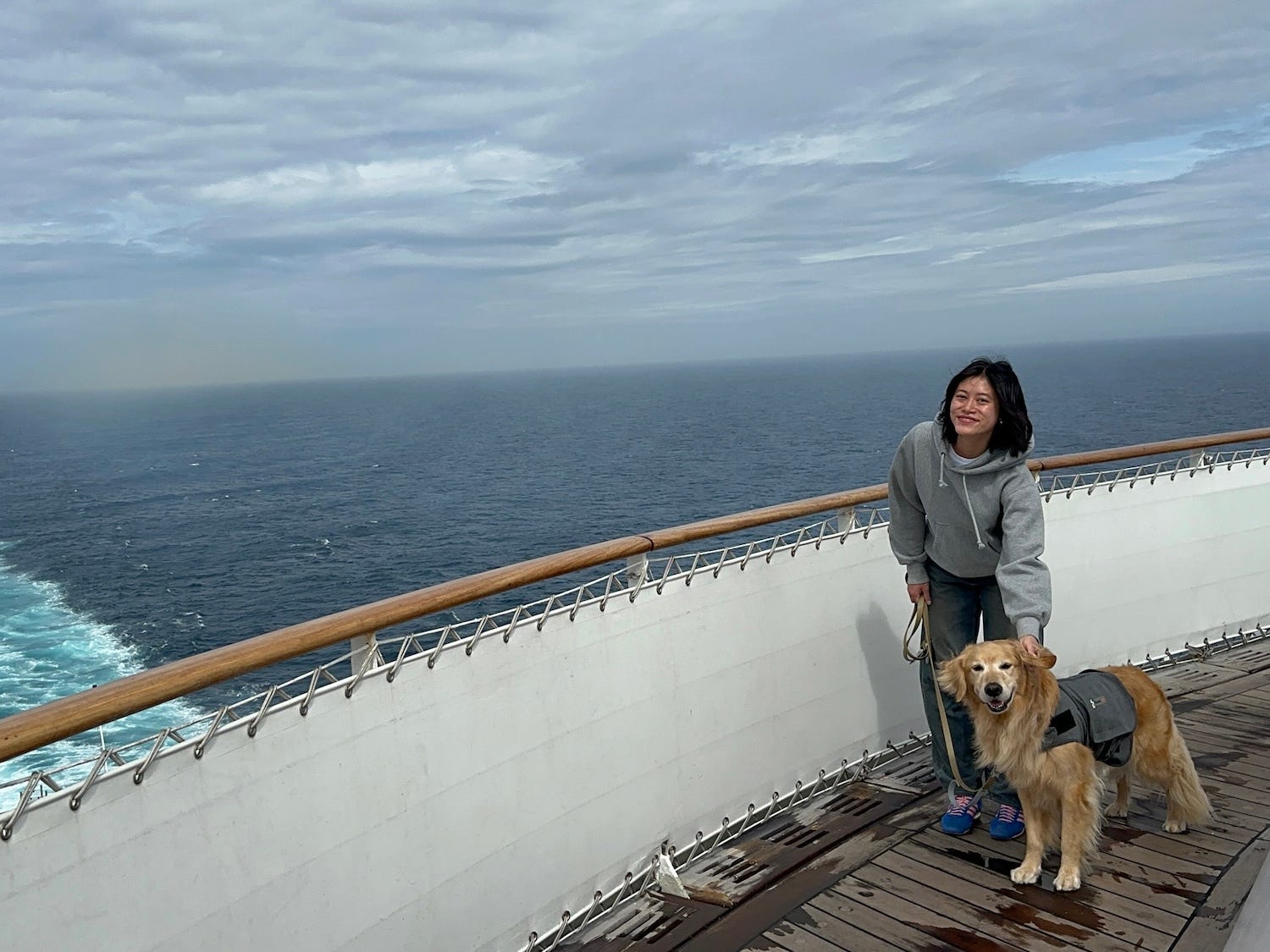 A woman and her dog stand together on the deck of a cruise.