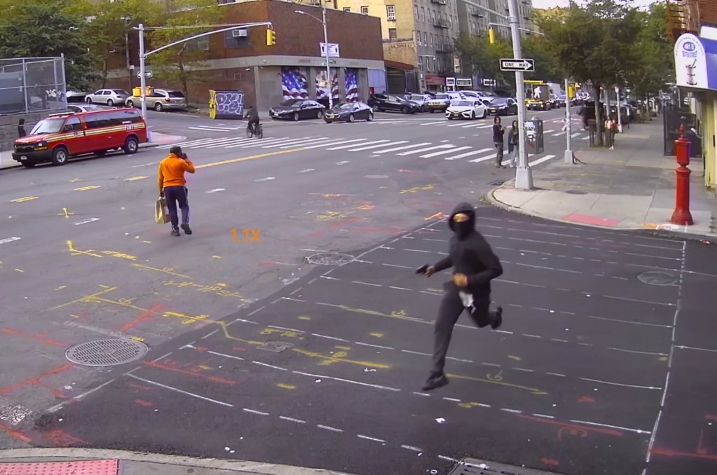 Surveillance footage of a ski mask-wearing gunman running through a street while holding a firearm.