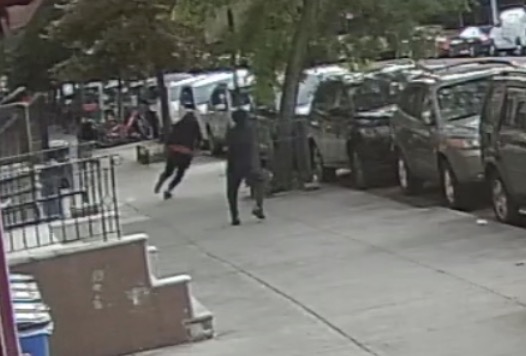Surveillance video of a ski mask-wearing gunman running after another person on a sidewalk.