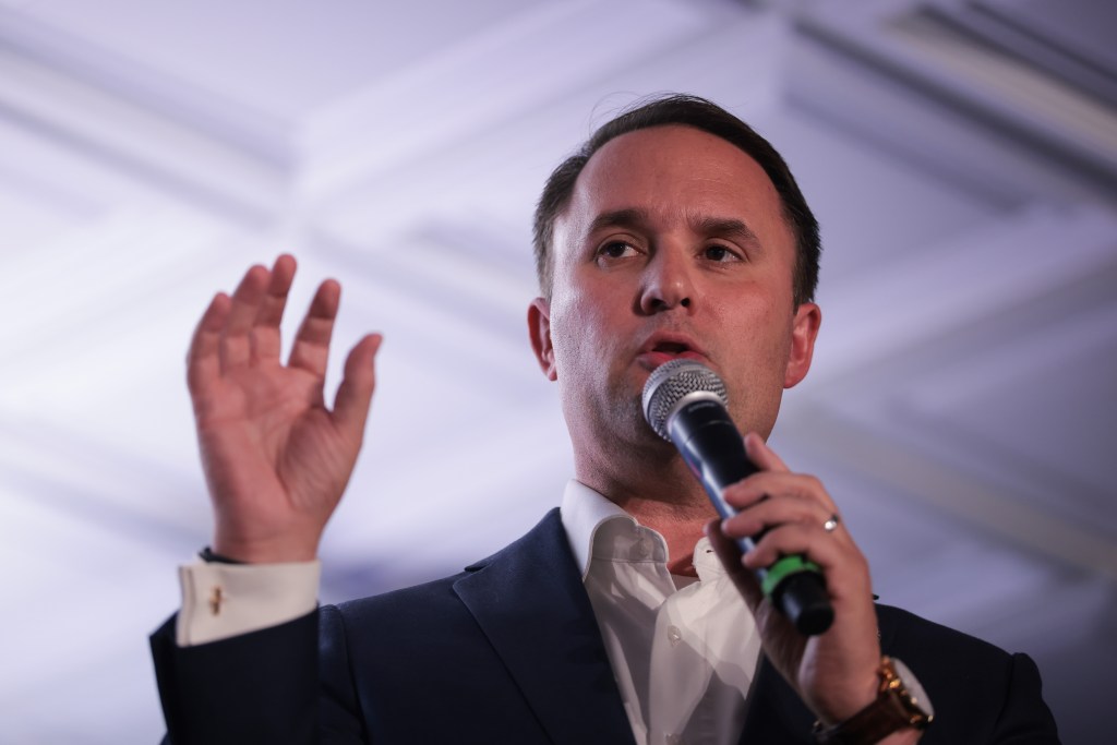 Virginia Attorney General Jason Miyares speaking into a microphone with his right hand raised.
