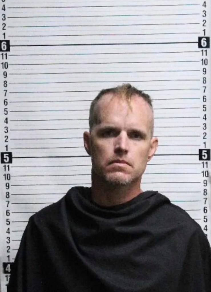 Mugshot of Nigel Edge, a man with short, thinning hair and a goatee, wearing a dark shirt, against a height chart.