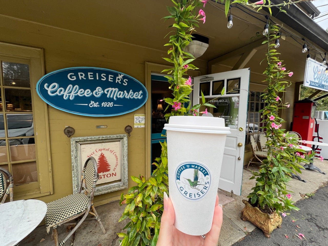 Hand holding coffee cup in front of Greisers storefront