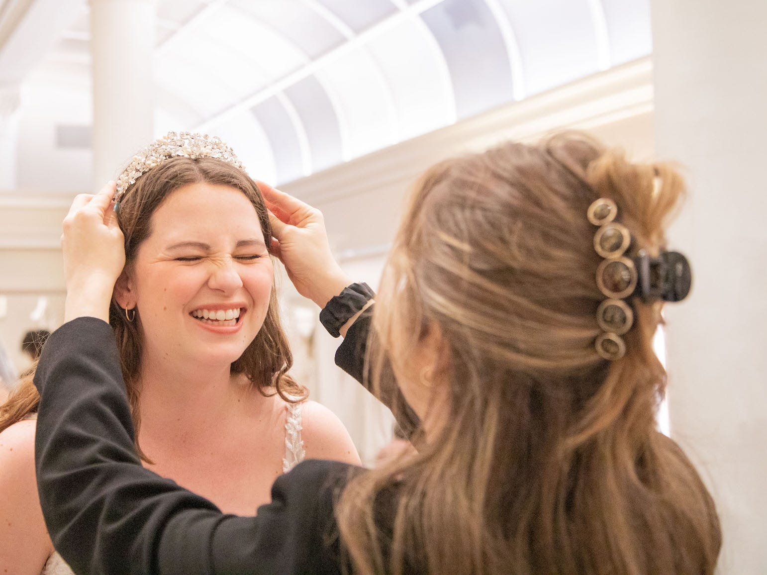 A bridal consultant puts a tiara on a woman at a bridal boutique.