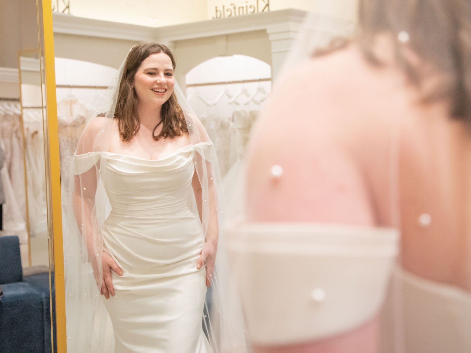 A woman in a wedding dress and a veil looks at herself in a mirror.
