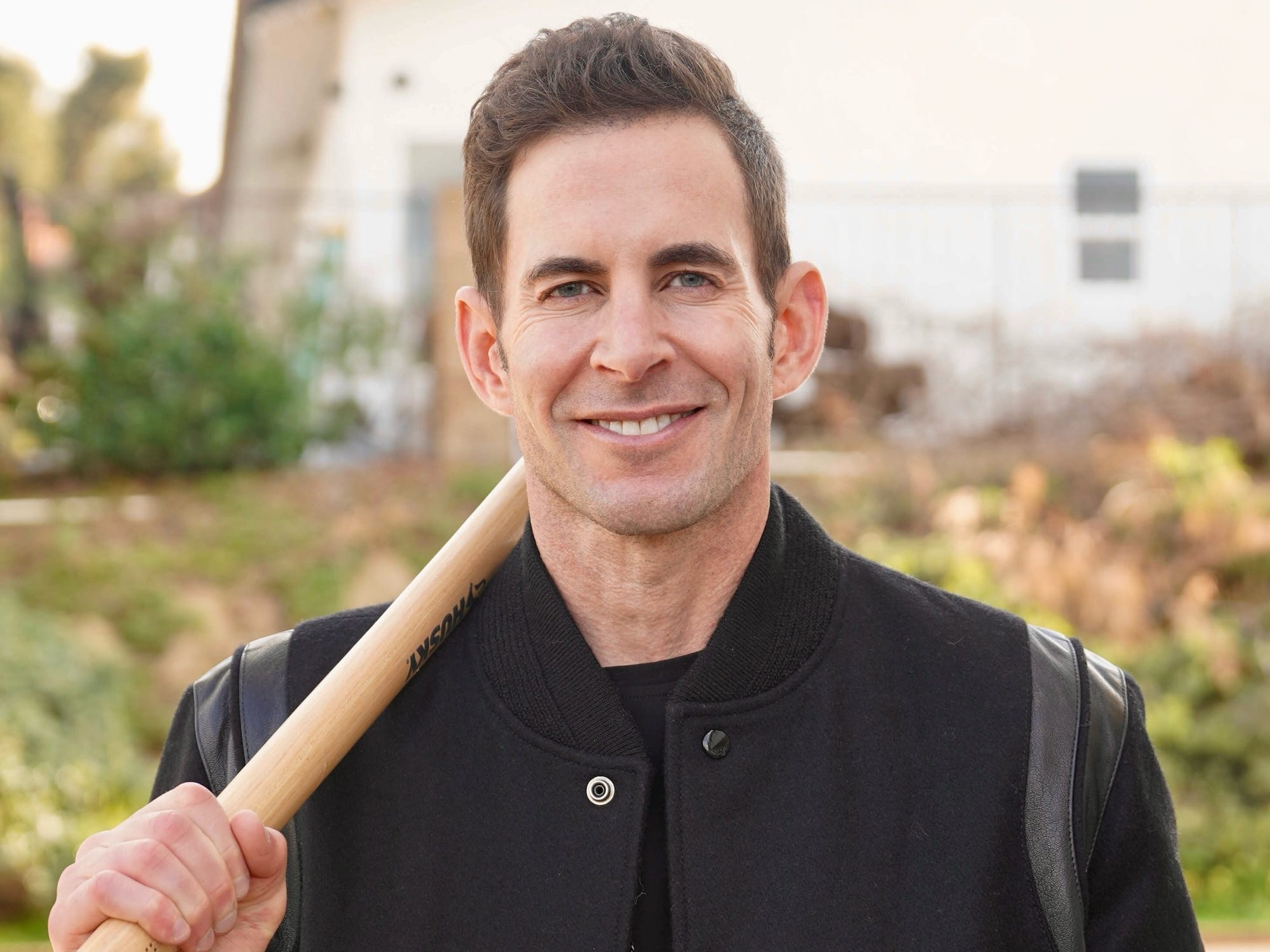 Tarek El Moussa smiles with a tool hanging over his shoulder.