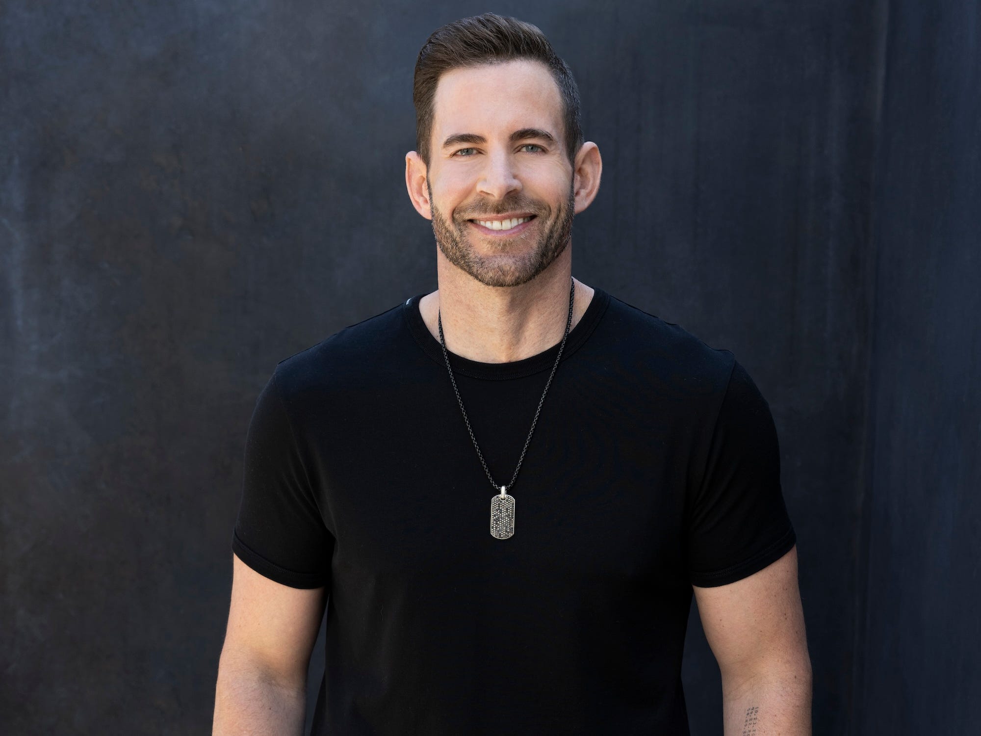 Tarek El Moussa smiles in front of a black wall.