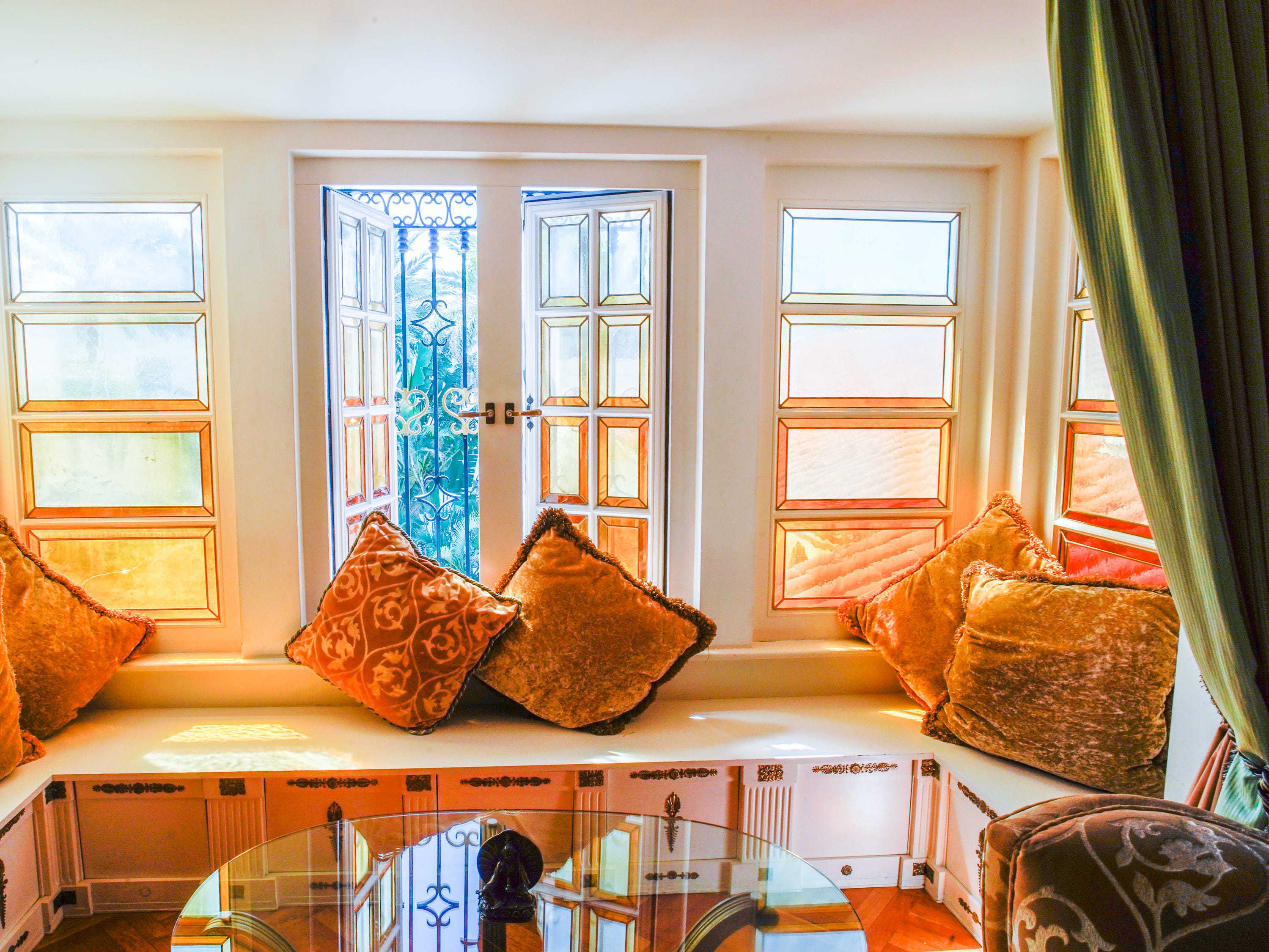 A view of a bench and glass table in front of stained-glass windows in the Aurora Suite in the former Versace Mansion