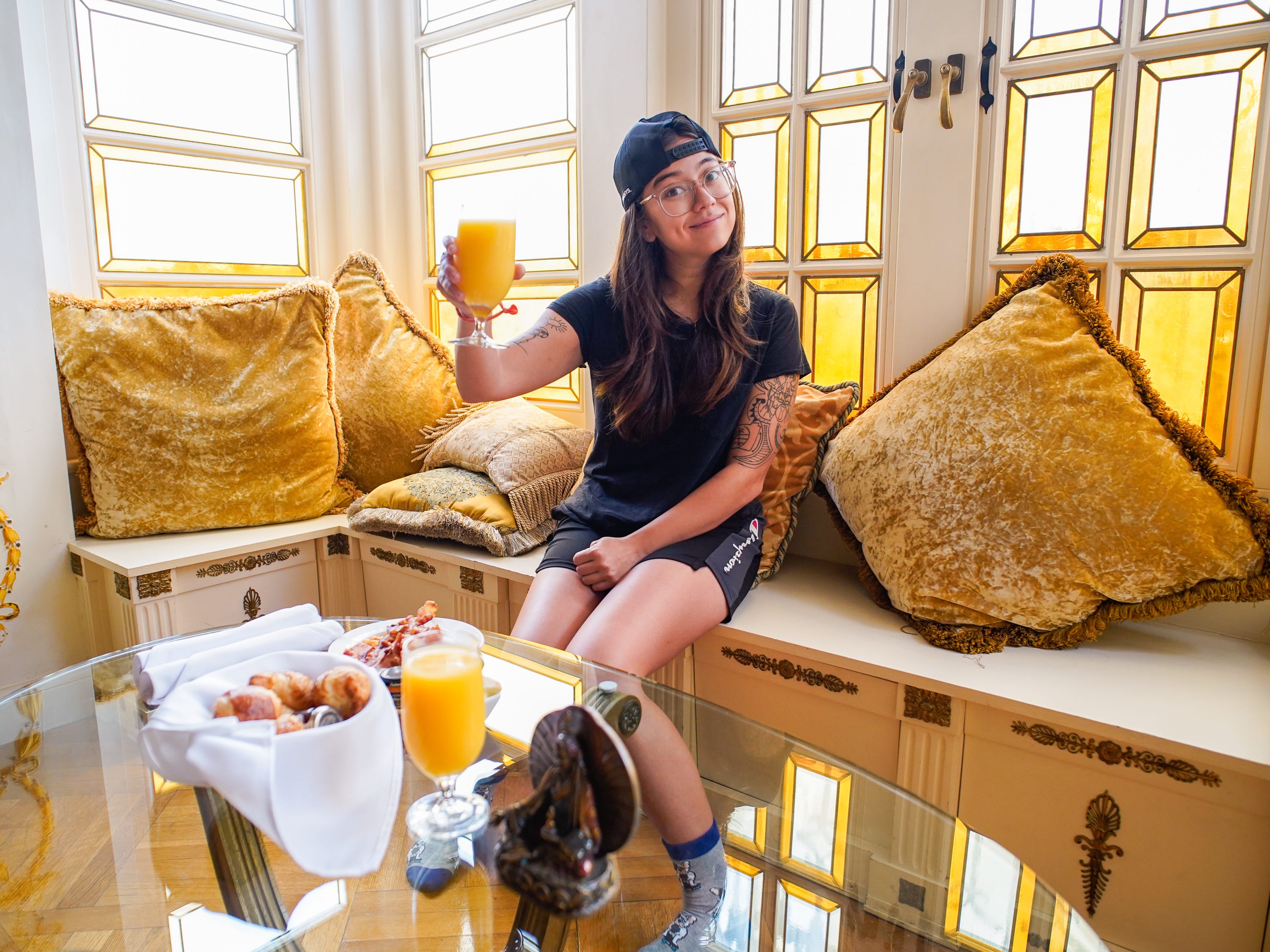 The author holds orange juice in the air in front of her breakfast in the former versace mansion