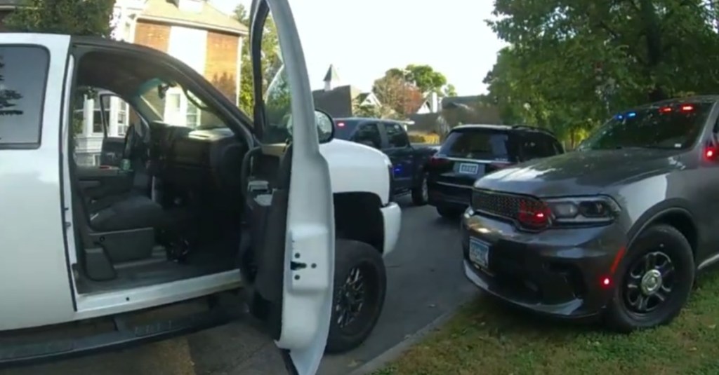 A white pickup truck with an open door and a police vehicle with flashing lights.