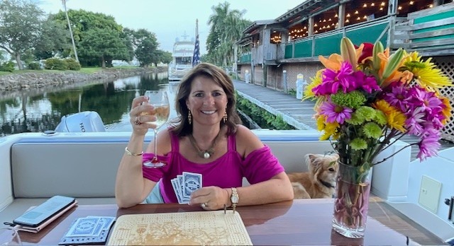 Linda Murphy smiling, holding a glass of white wine and playing cards on a boat.