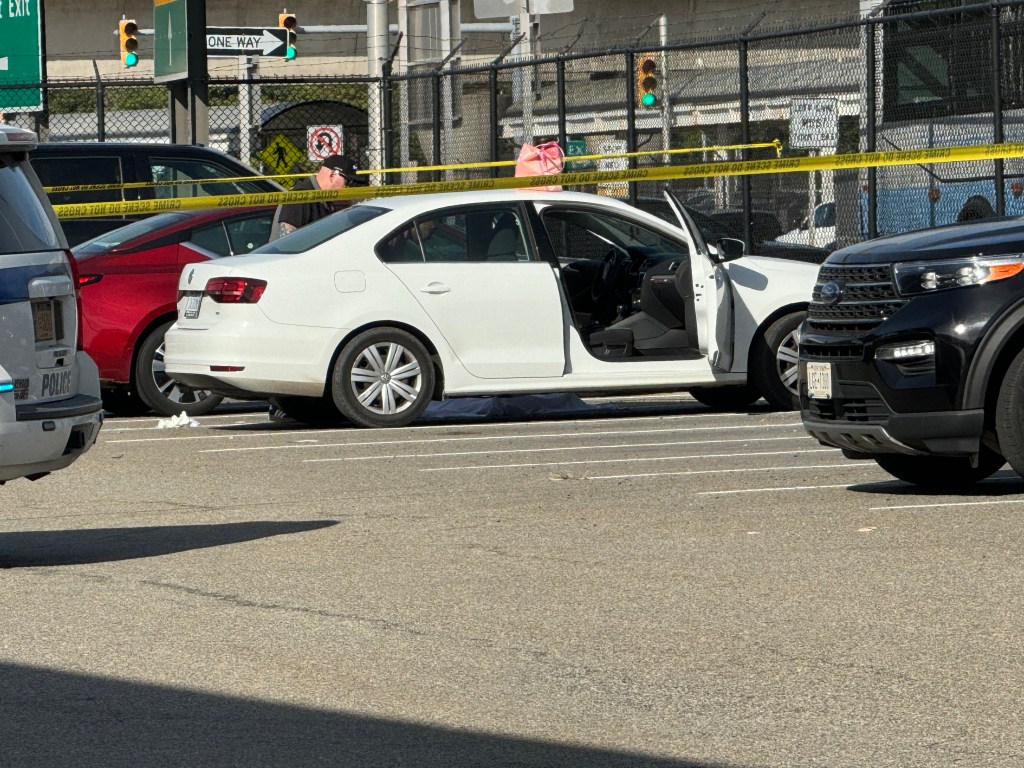 Body found in a parking lot, surrounded by yellow crime scene tape and several vehicles, including a police car.