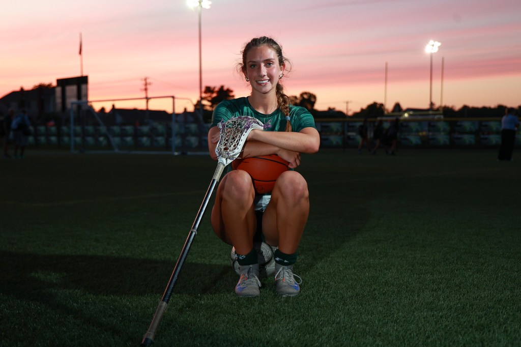 Madison Reedy, a junior at Carle Place H.S. and three-sport star, posing with a lacrosse stick and basketball on a field at dusk.