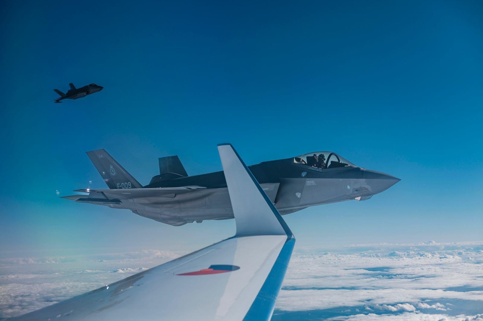 Dutch F-35 stealth fighter jets fly alongside an aircraft.